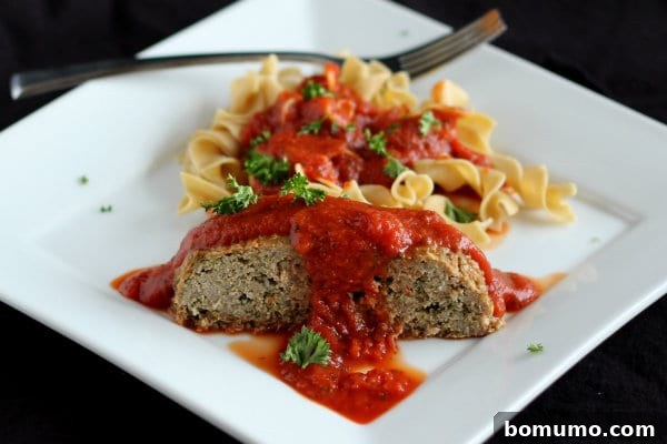 A close-up serving of Heart-Healthy Italian Turkey Quinoa Meatloaf on a square white plate, with a fork gently resting beside it. The dish is accompanied by a luscious marinara sauce and whole grain noodles, showcasing a simple yet inviting presentation of a nutritious meal.
