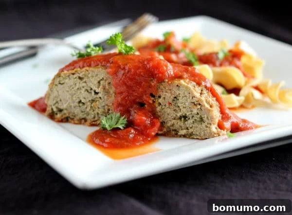 Front view of a beautifully presented serving of Heart-Healthy Italian Turkey Quinoa Meatloaf on a pristine white plate, accompanied by savory whole grain noodles and rich marinara sauce. This healthy, flavorful meal is ready to be enjoyed.