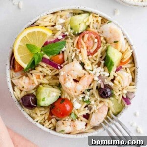 A perfectly portioned Greek orzo salad with shrimp, olives, and tomatoes, presented in a square format.