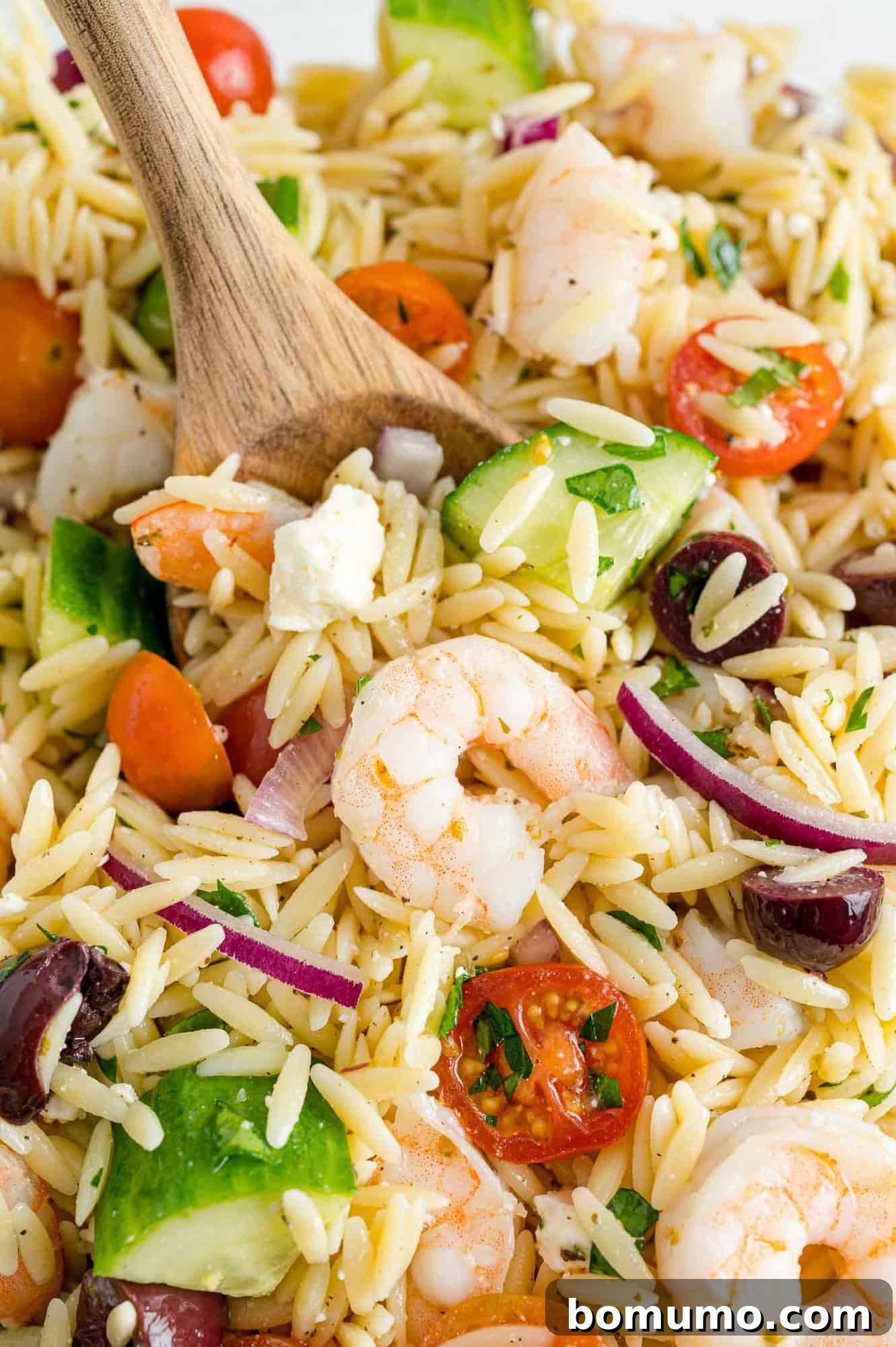 Close-up shot of a forkful of Greek orzo salad, highlighting the fresh mint, lemon, and parsley, suggesting a satisfying, light meal.