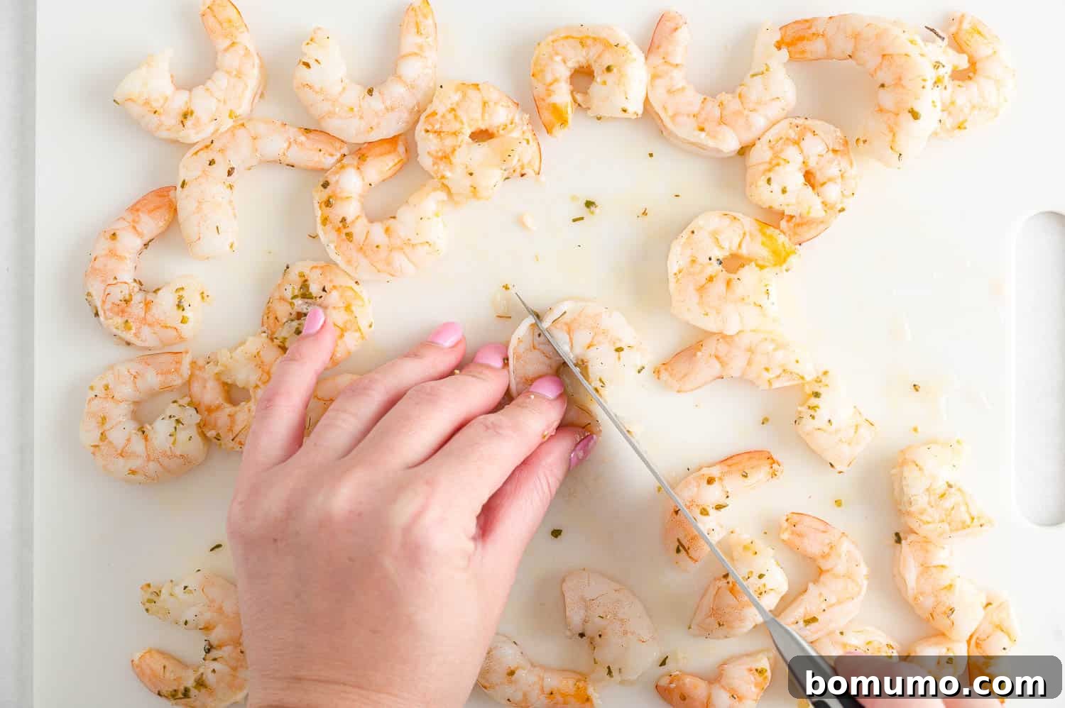 A close-up shot of cooked shrimp being roughly chopped on a cutting board, preparing it for inclusion in the orzo salad.