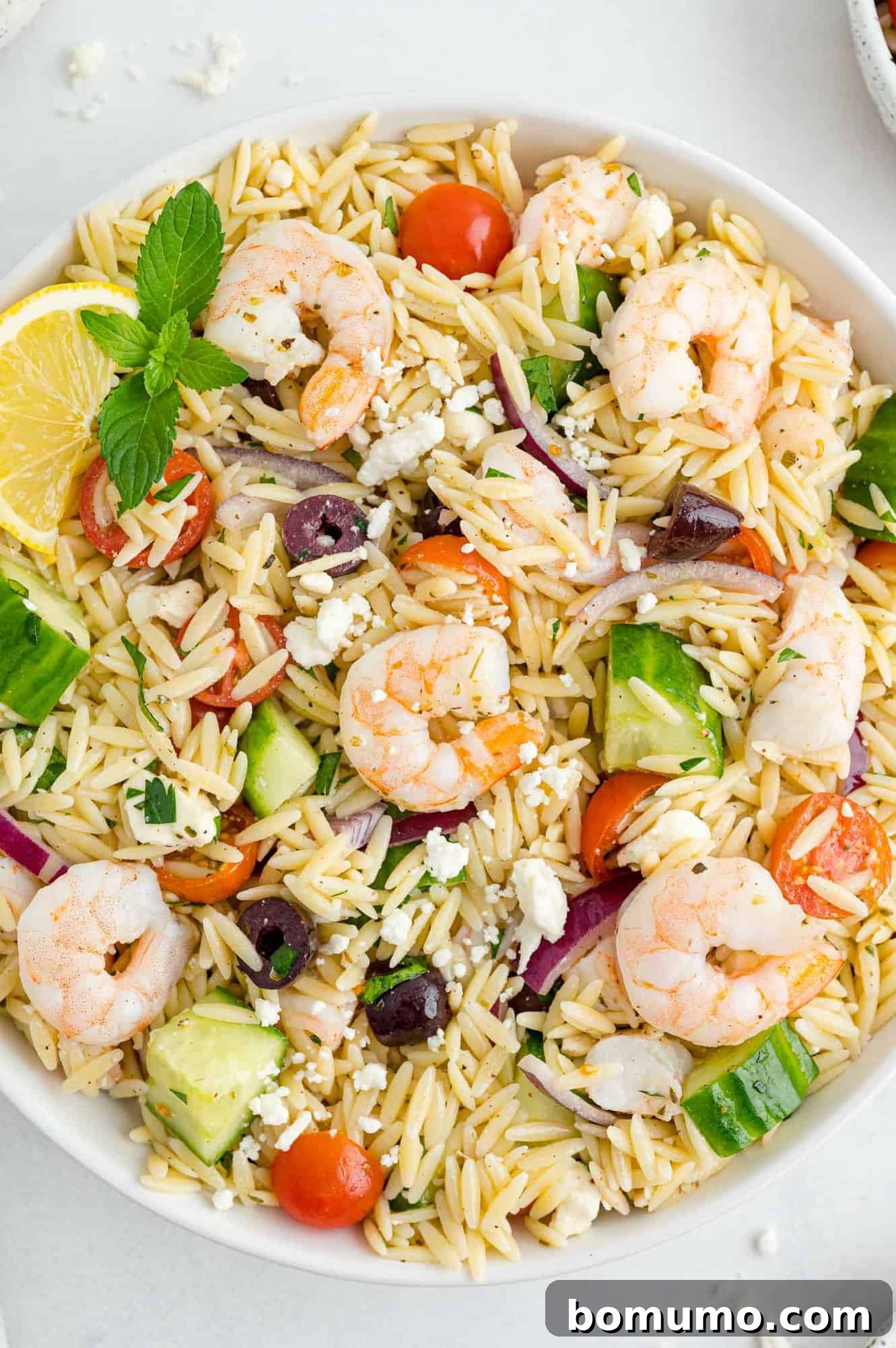 A large, inviting serving bowl filled with Greek orzo salad, showcasing plump shrimp, briny olives, colorful tomatoes, crisp onions, and crumbled feta cheese.