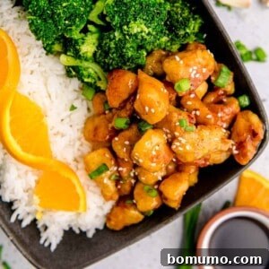 Orange chicken on a black plate with broccoli and rice.