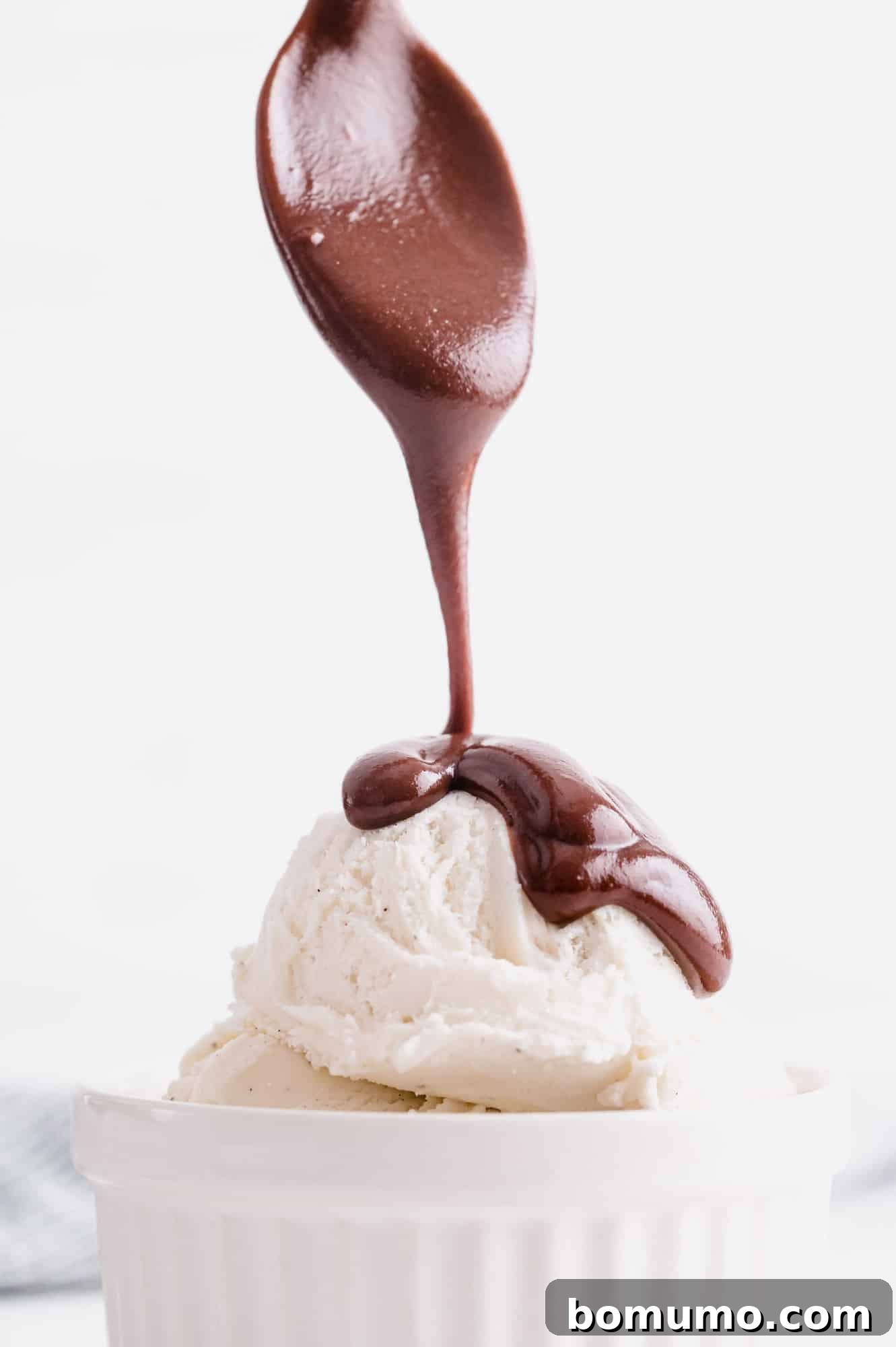 Homemade hot fudge being poured generously over a scoop of vanilla ice cream, creating a delightful dessert.