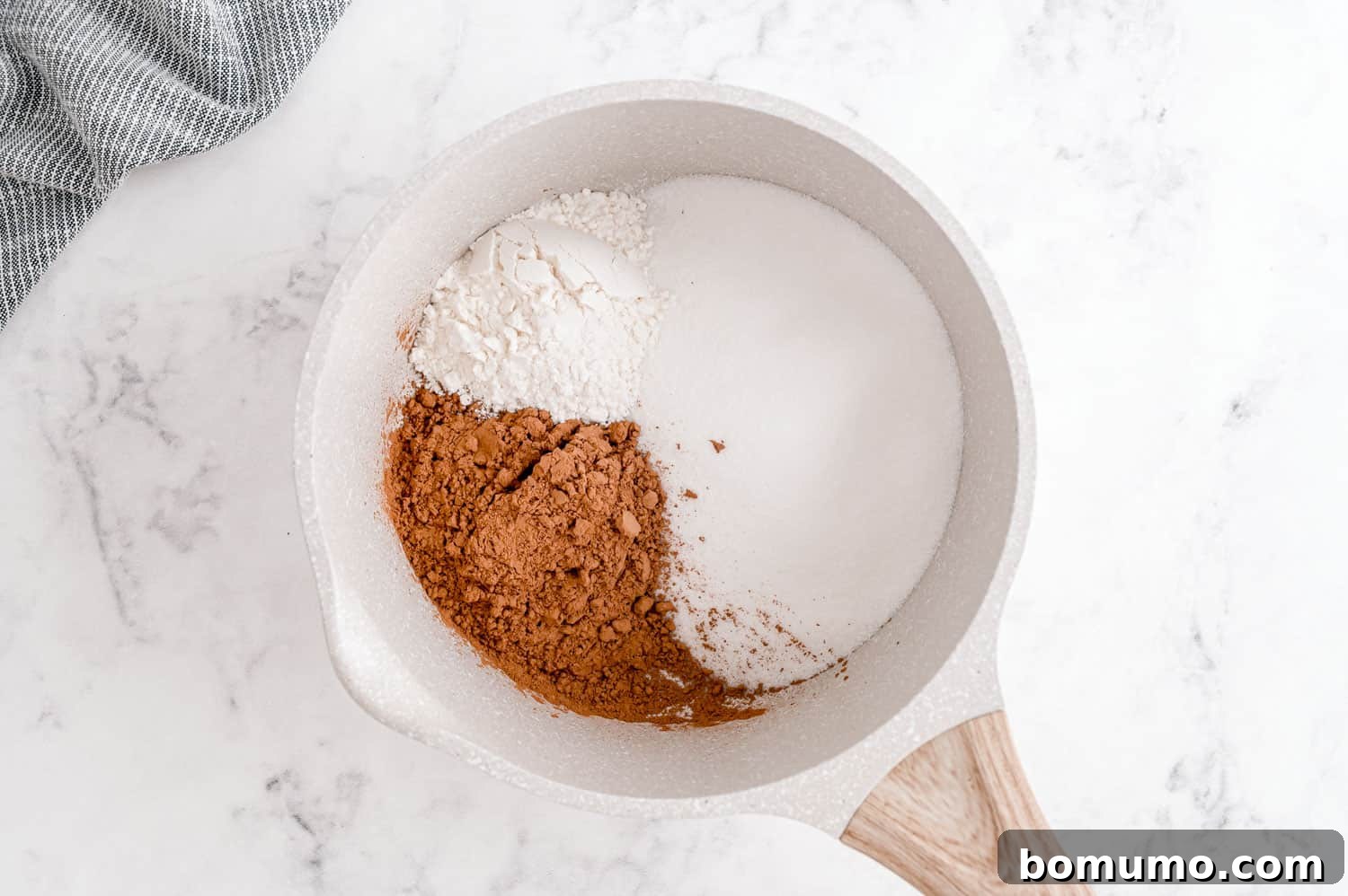 Dry ingredients like sugar, cocoa, and flour mixed together in a saucepan before liquids are added.