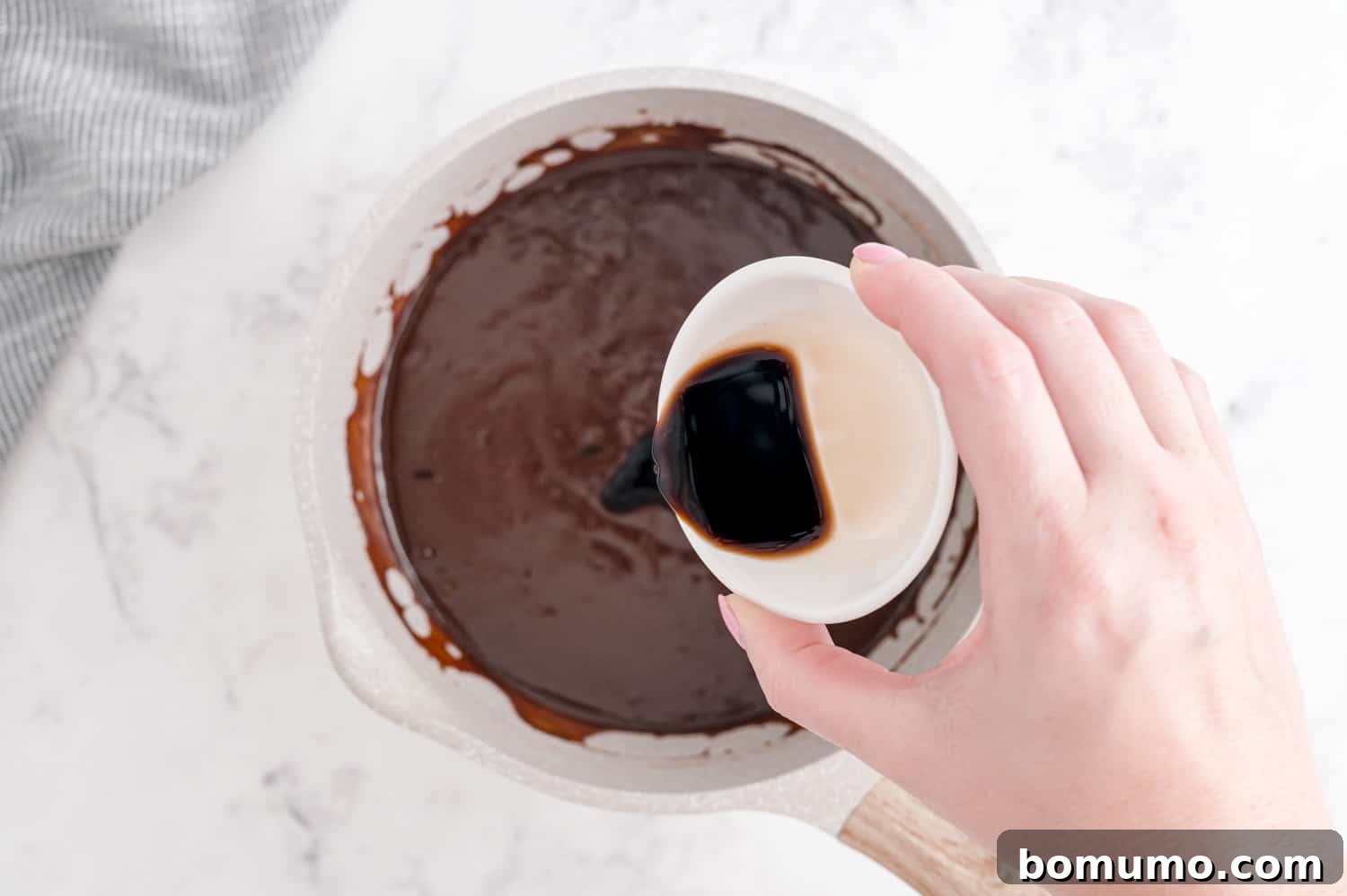 Pure vanilla extract being poured into the freshly cooked hot fudge sauce, adding its final aromatic touch.