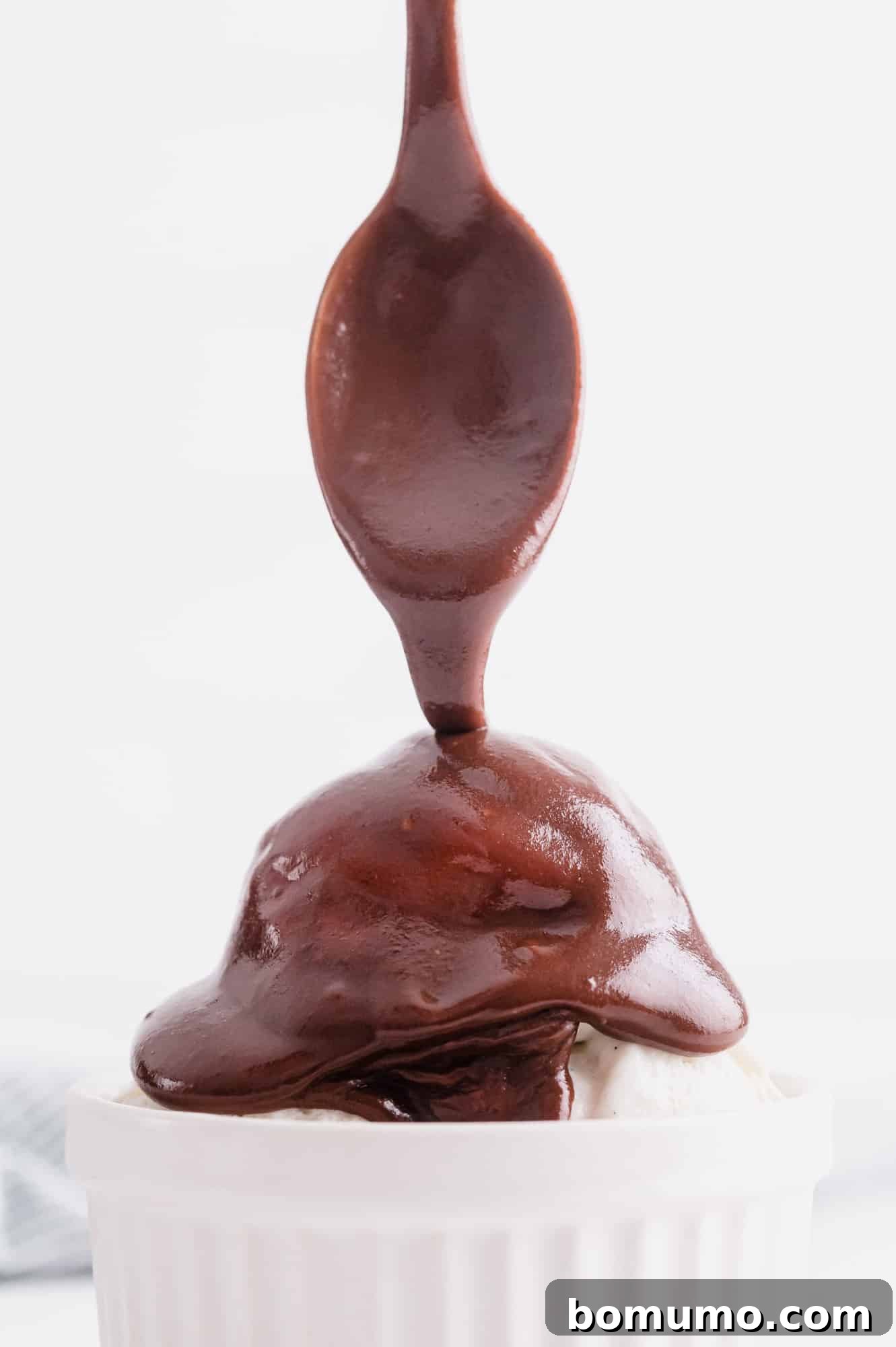 Rich chocolate hot fudge sauce being generously drizzled over a bowl of ice cream, adorned with colorful M&Ms.