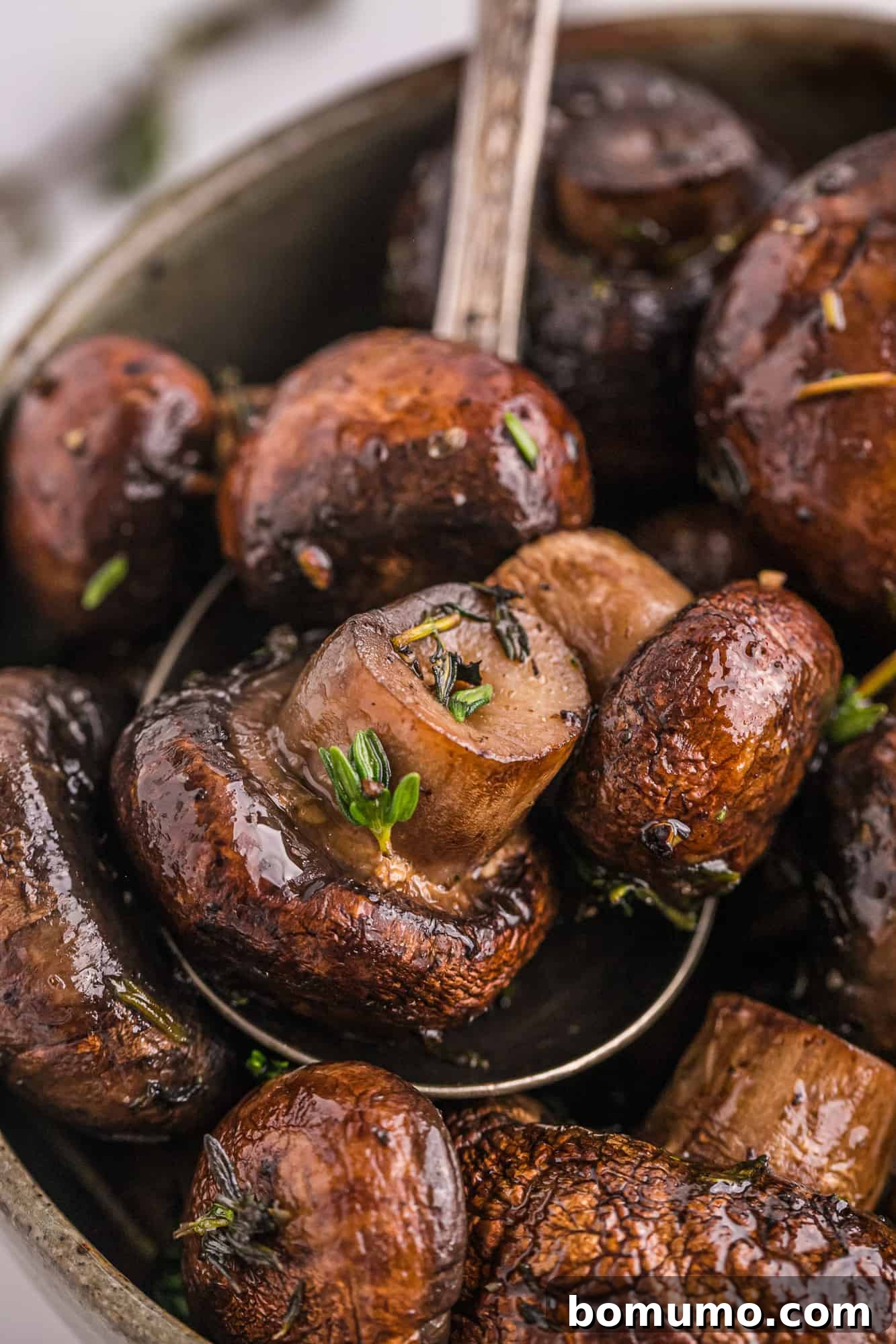 Umami Roasted Mushrooms 3 Close-up of succulent roasted mushrooms being scooped from a serving bowl with a spoon, highlighting their tender, golden-brown texture.