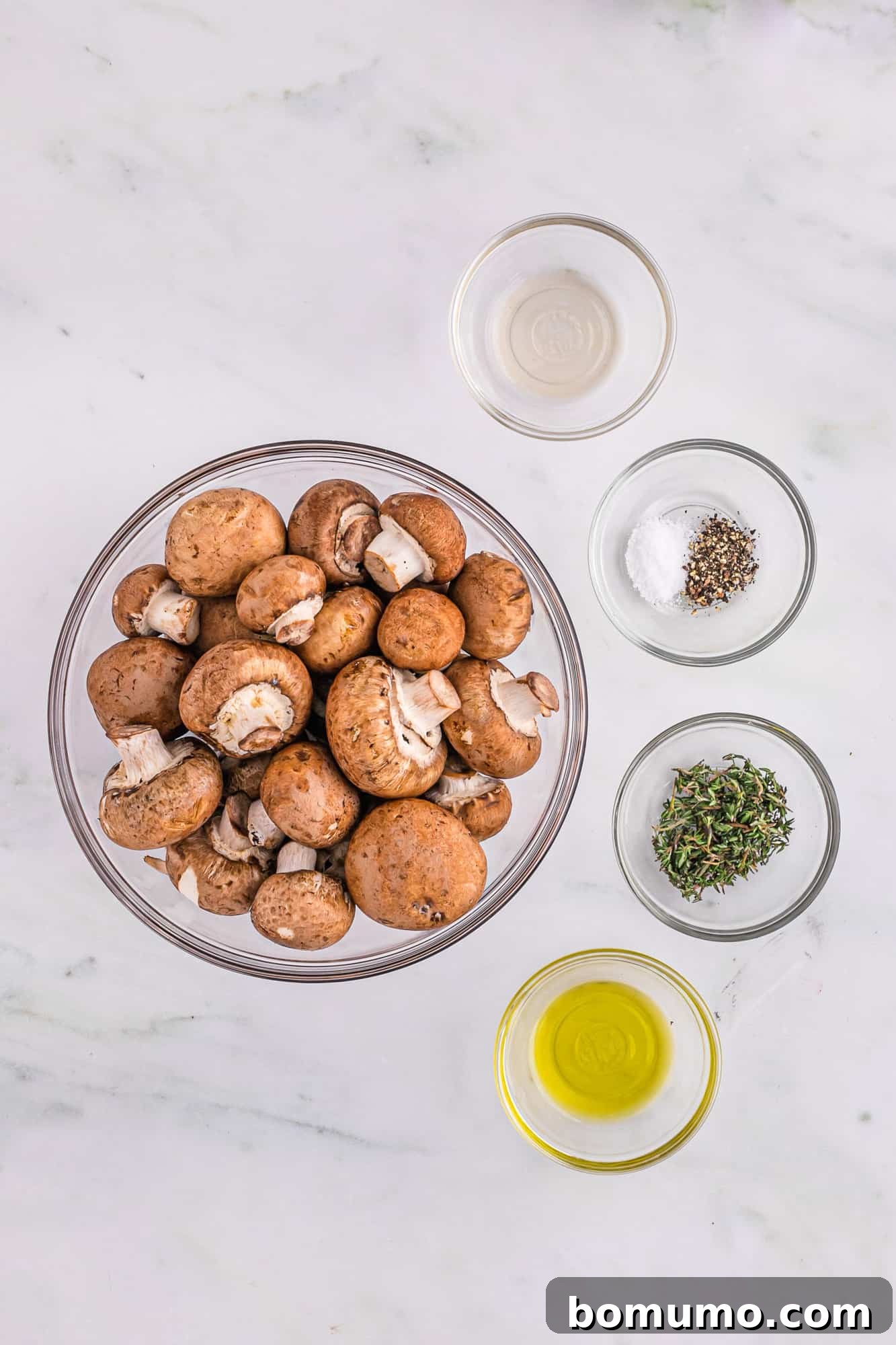 Umami Roasted Mushrooms 4 A collection of fresh ingredients for perfectly roasted mushrooms: whole cremini mushrooms, a bottle of olive oil, balsamic vinegar, fresh thyme sprigs, and salt and pepper grinders.