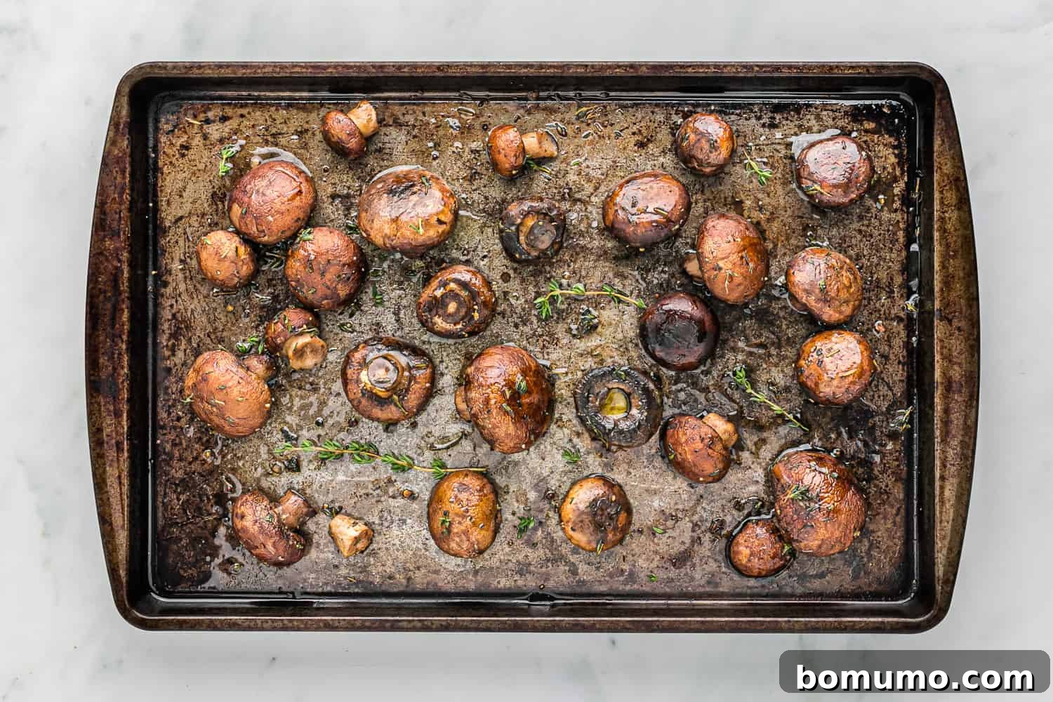 Umami Roasted Mushrooms 7 Freshly roasted mushrooms on a baking sheet, glistening with caramelized balsamic glaze and sprinkled with vibrant fresh thyme, ready to be enjoyed.