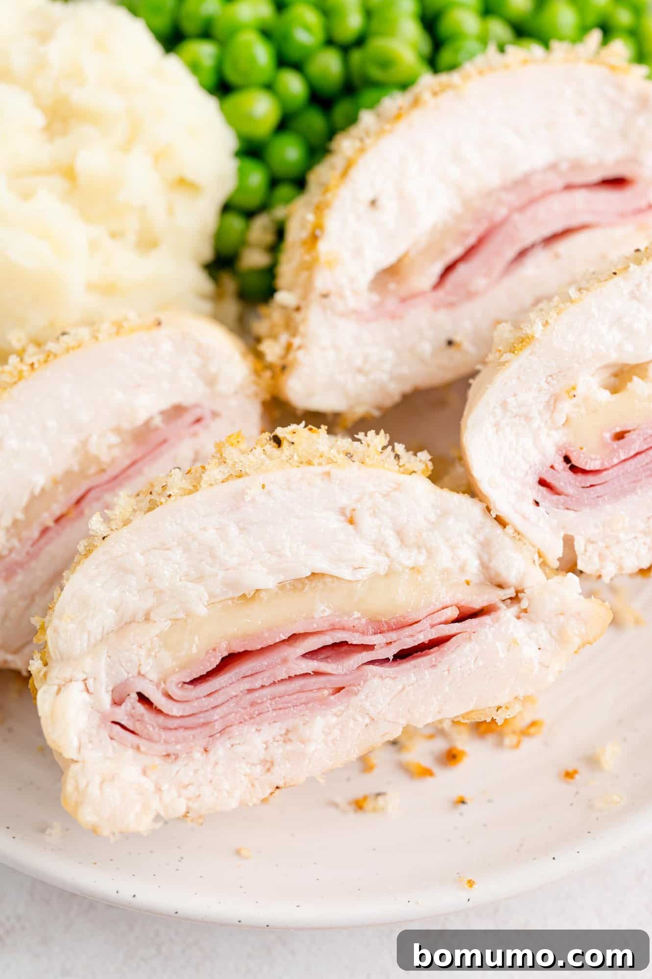 A freshly baked chicken cordon bleu, sliced and presented on a white plate, showcasing its golden-brown crust and melted cheese filling.