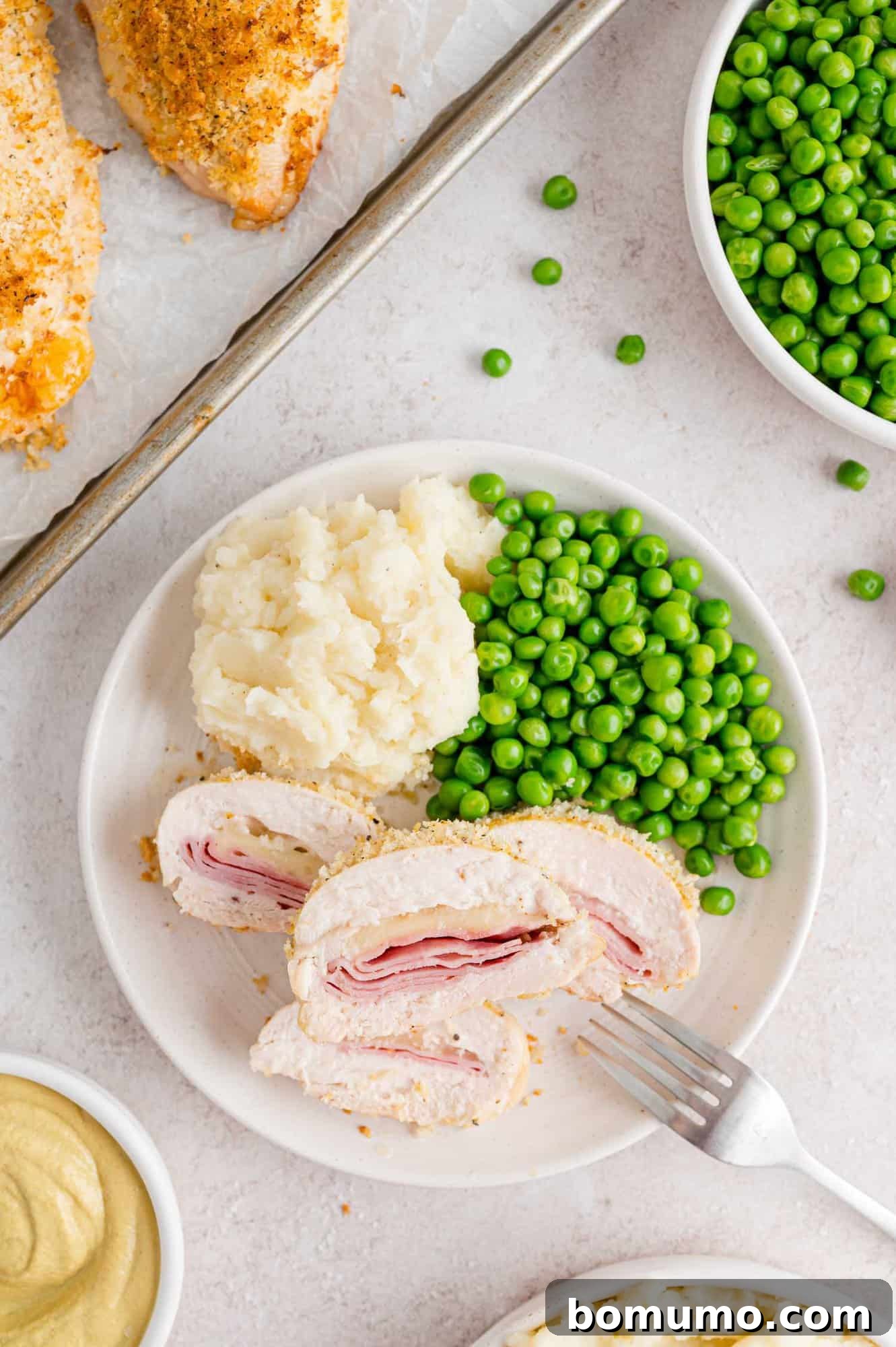 Sliced baked chicken cordon bleu revealing the rich ham and Swiss cheese filling, served on a plate with fresh peas and roasted potatoes.