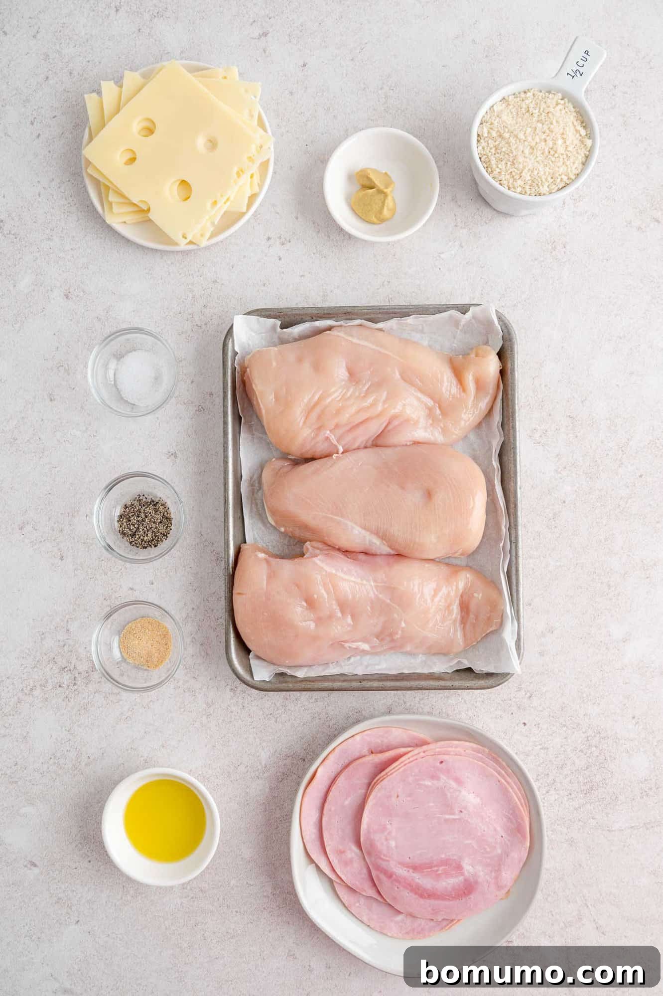 Ingredients for baked chicken cordon bleu laid out, including chicken breasts, slices of Swiss cheese, and deli ham.