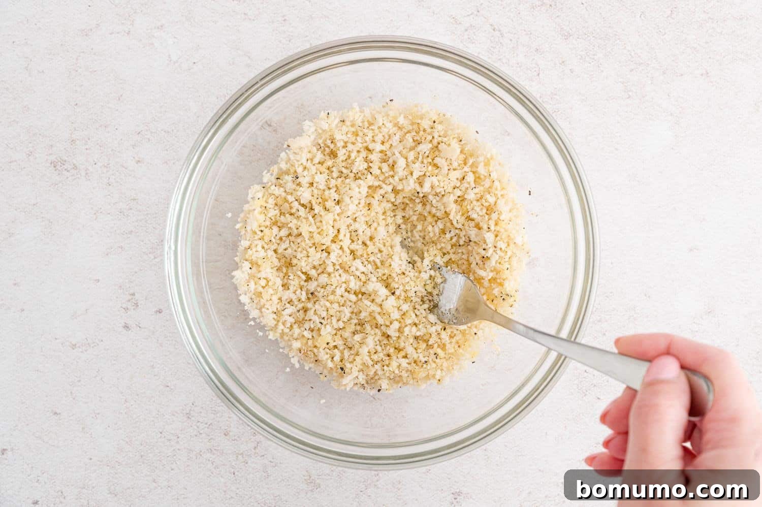 Panko bread crumbs being mixed with seasonings and olive oil in a bowl.