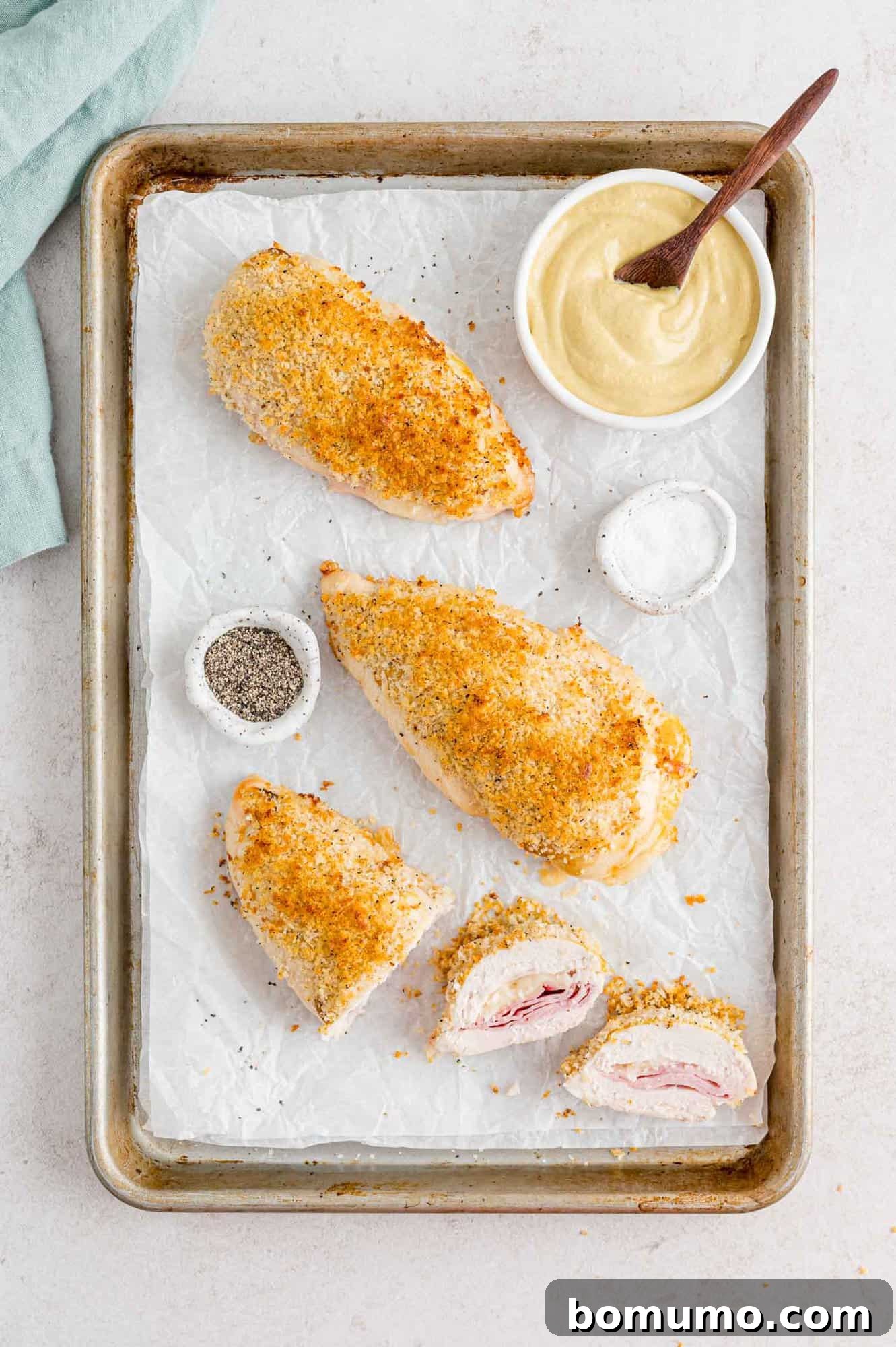 Several pieces of baked chicken cordon bleu neatly arranged on a sheet pan, showcasing their golden-brown crust.