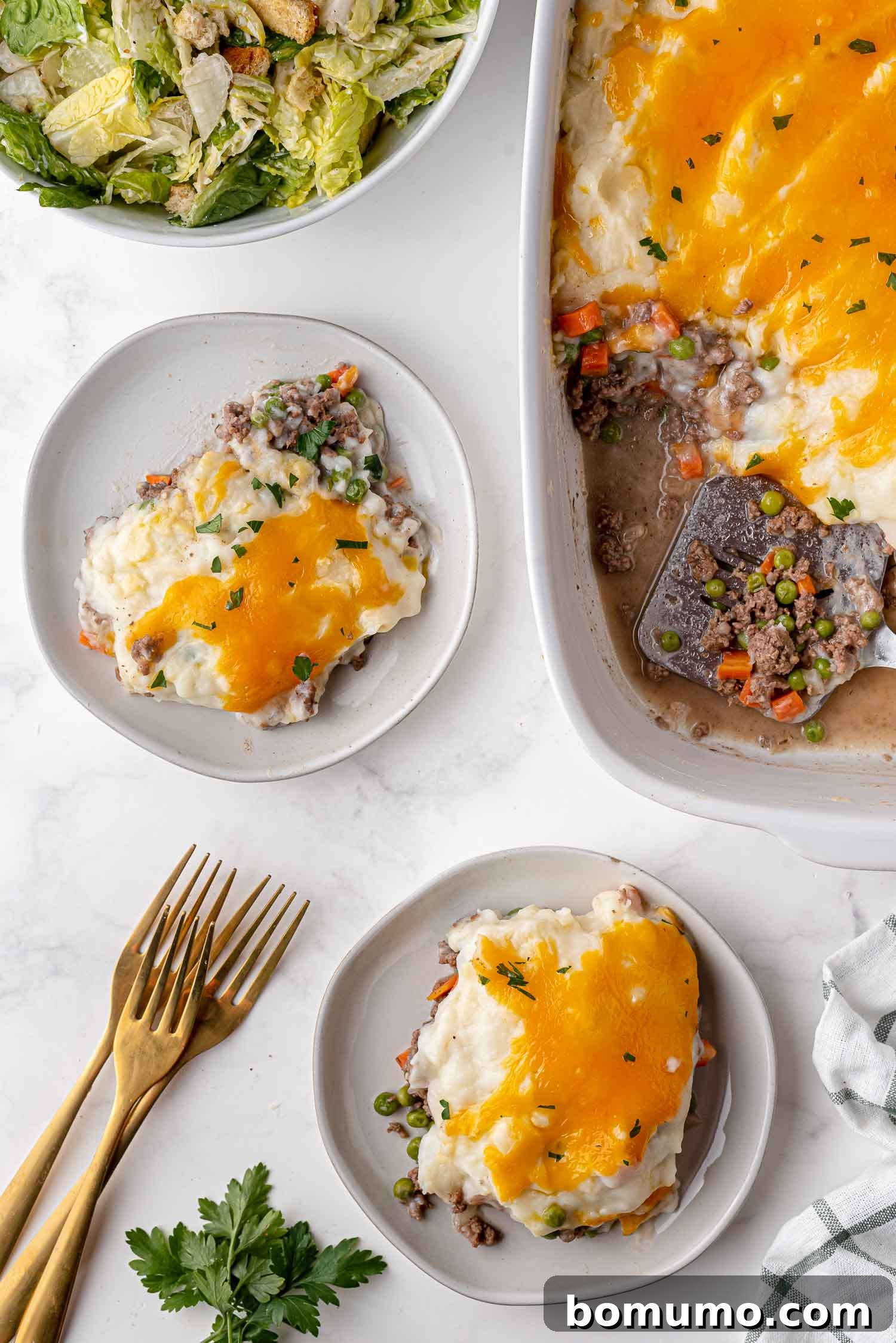 An inviting overhead shot showcasing two beautifully plated portions of shepherd's pie alongside a full, bubbling casserole dish, highlighting the inviting golden crust and steaming, rich interior of the dish.