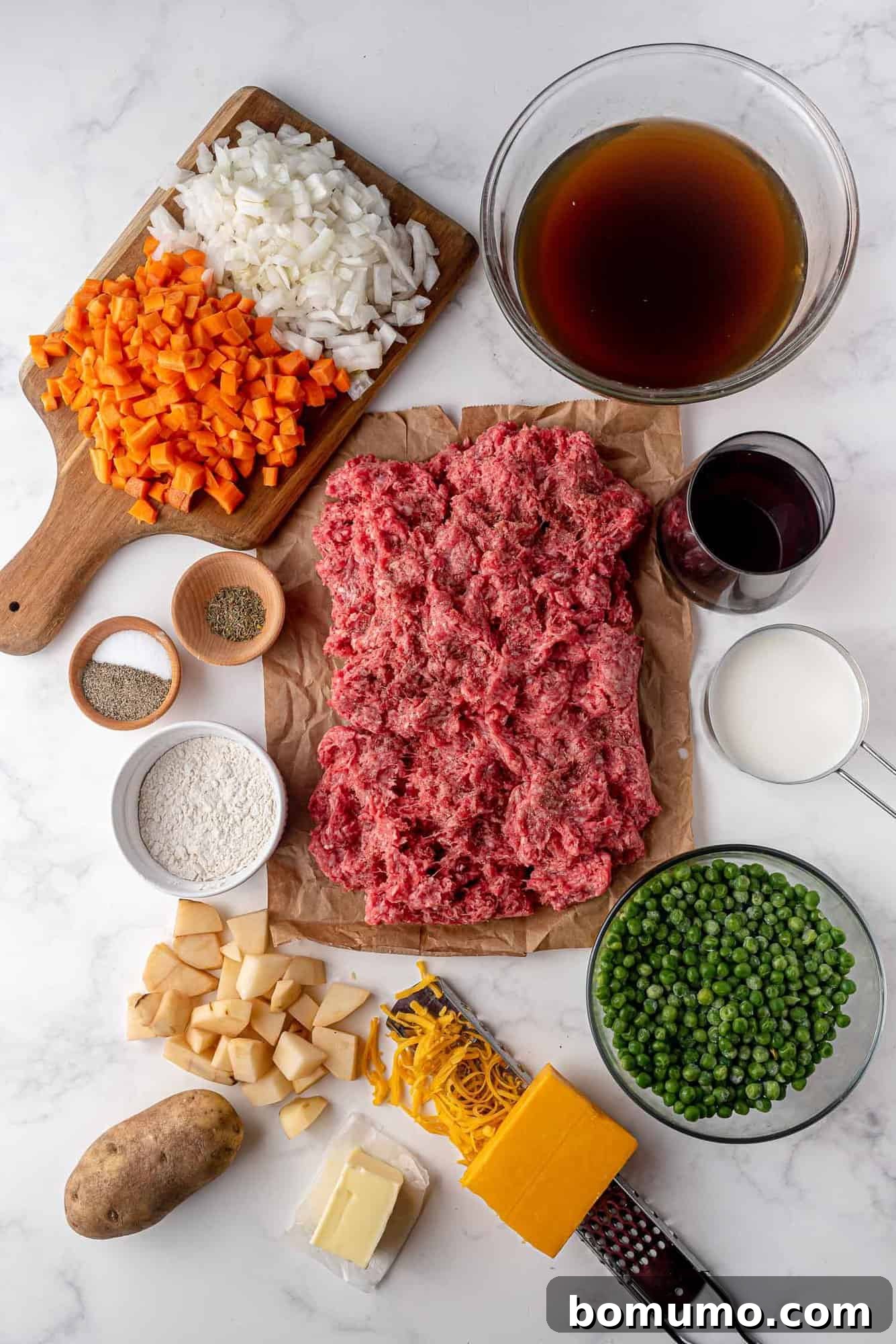 A vibrant display of fresh, high-quality ingredients meticulously arranged for Shepherd's Pie. The composition includes raw ground lamb, an assortment of colorful vegetables like carrots and onions, a bottle of dry red wine, a block of sharp cheddar cheese, whole potatoes, and fragrant seasoning herbs.