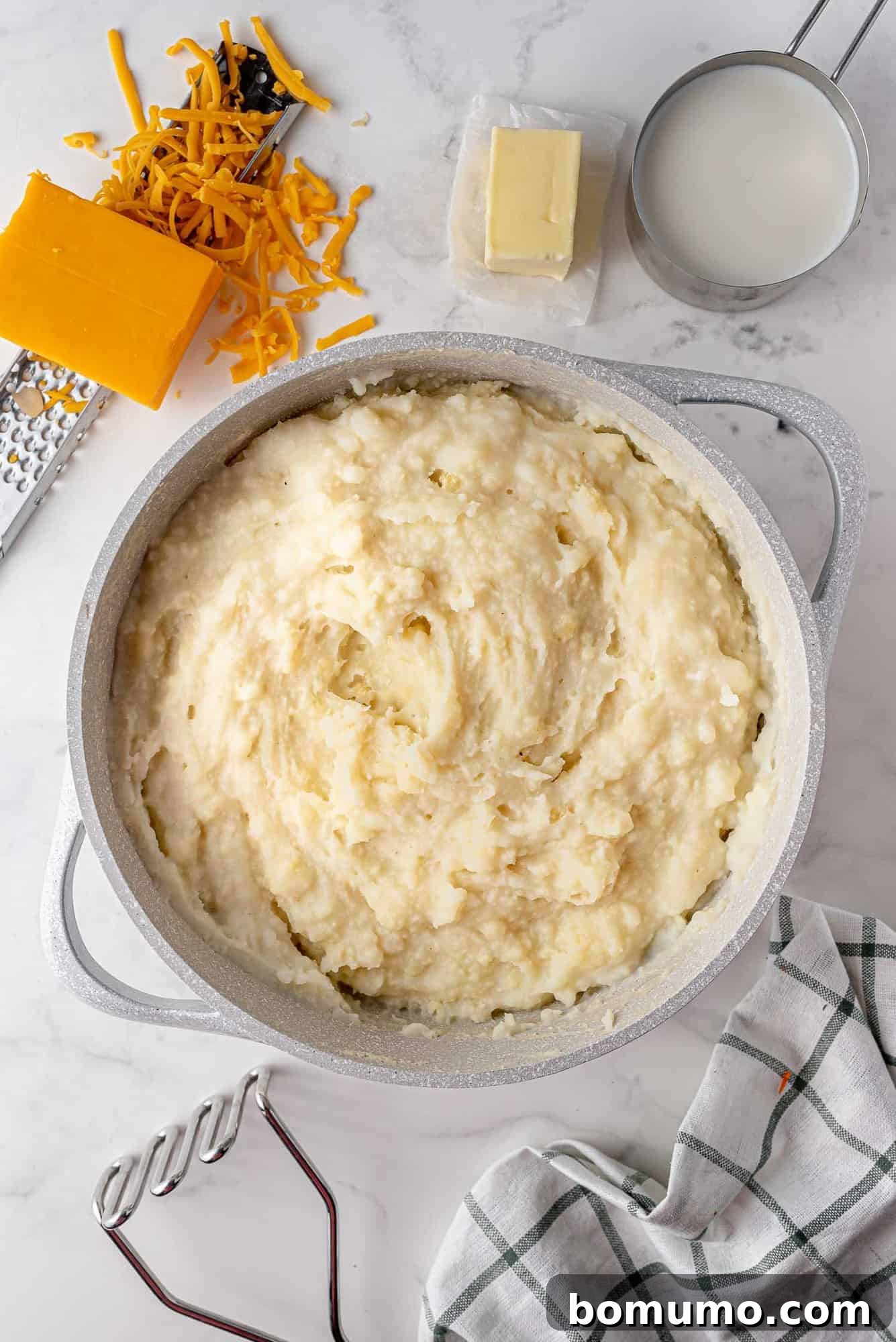 Creamy mashed potatoes, perfectly prepared and seasoned, ready to top a savory shepherd's pie filling, sit invitingly in a large pan after being mashed.