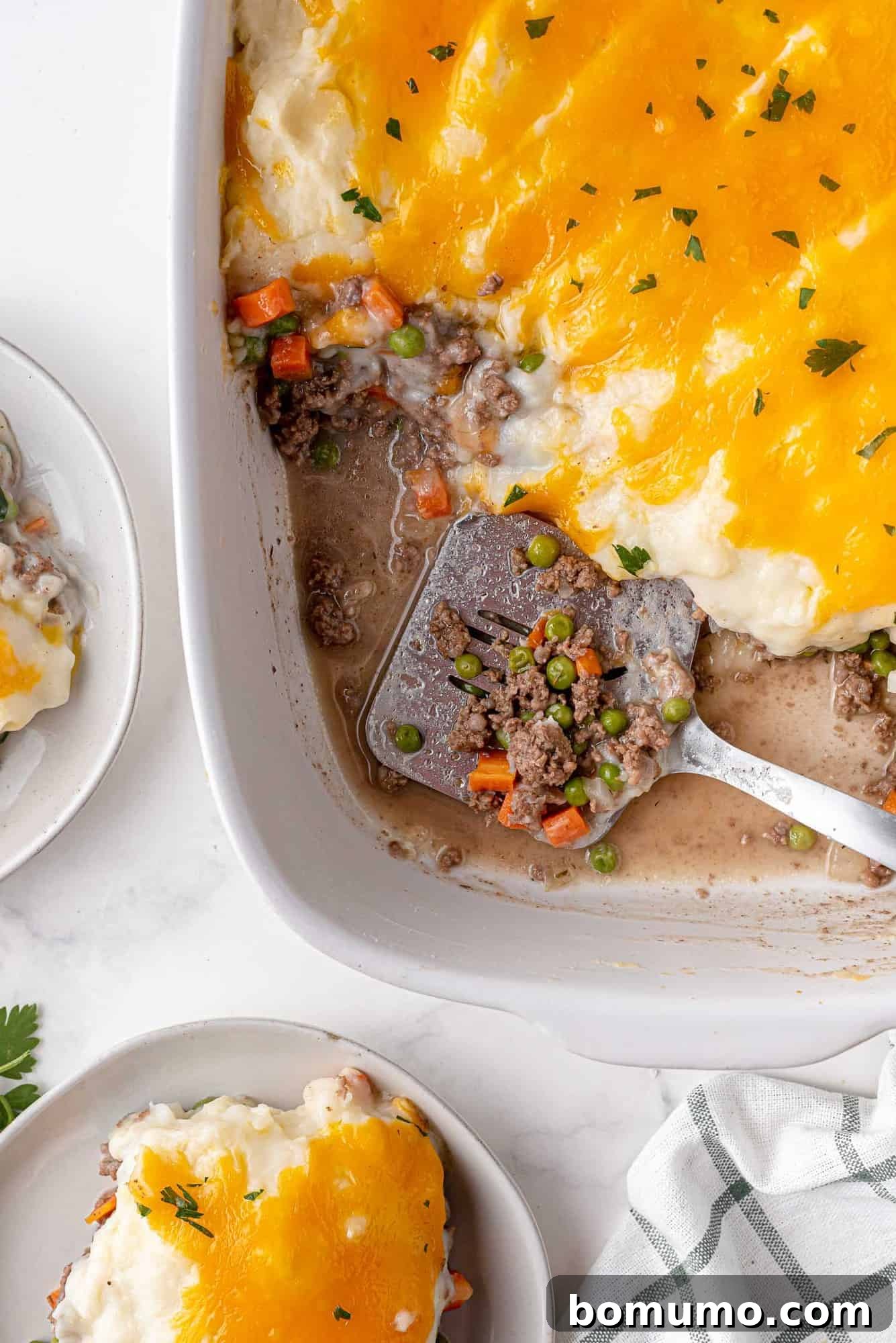 A large metal spatula carefully scooping a generous portion of freshly baked shepherd's pie from a white baking dish, showcasing the distinct layers of creamy mashed potato topping and savory lamb filling.