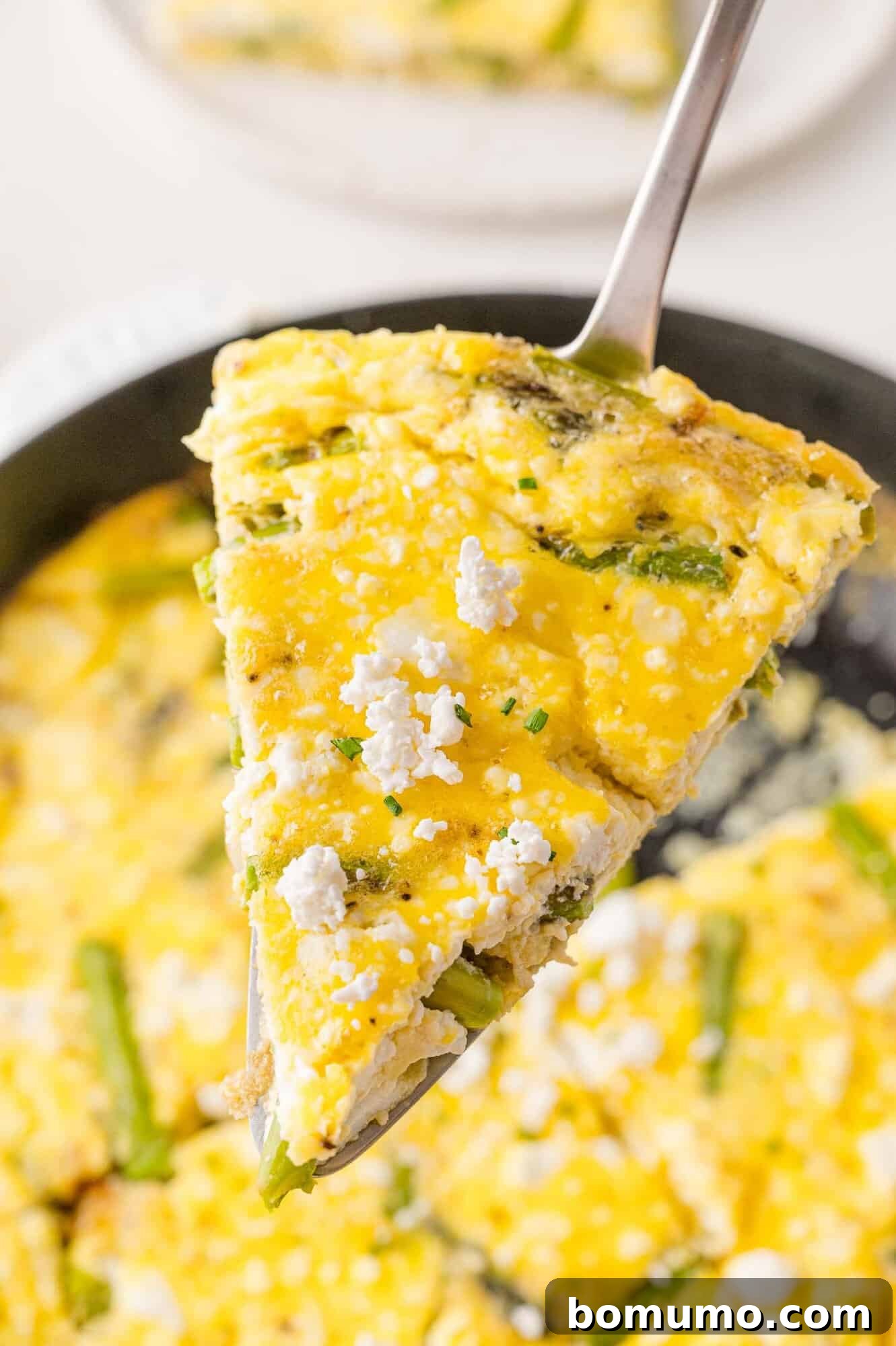 A golden-brown slice of vegetable frittata, showcasing asparagus and melted cheese, being delicately lifted from the pan with a spatula, ready to be enjoyed.