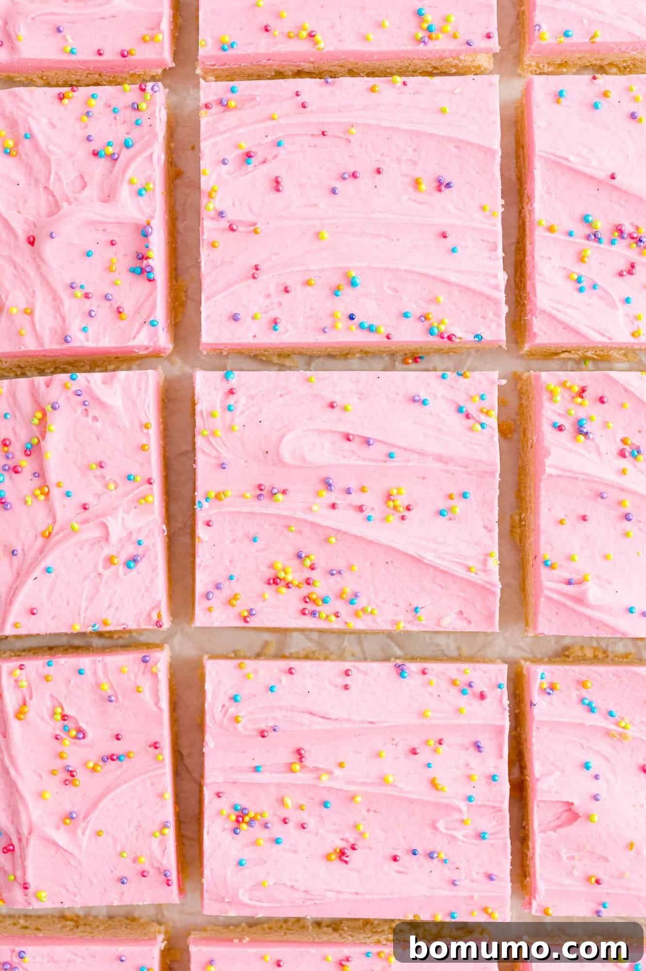 Cookie bars with pink frosting, viewed from above, adorned with colorful sprinkles.