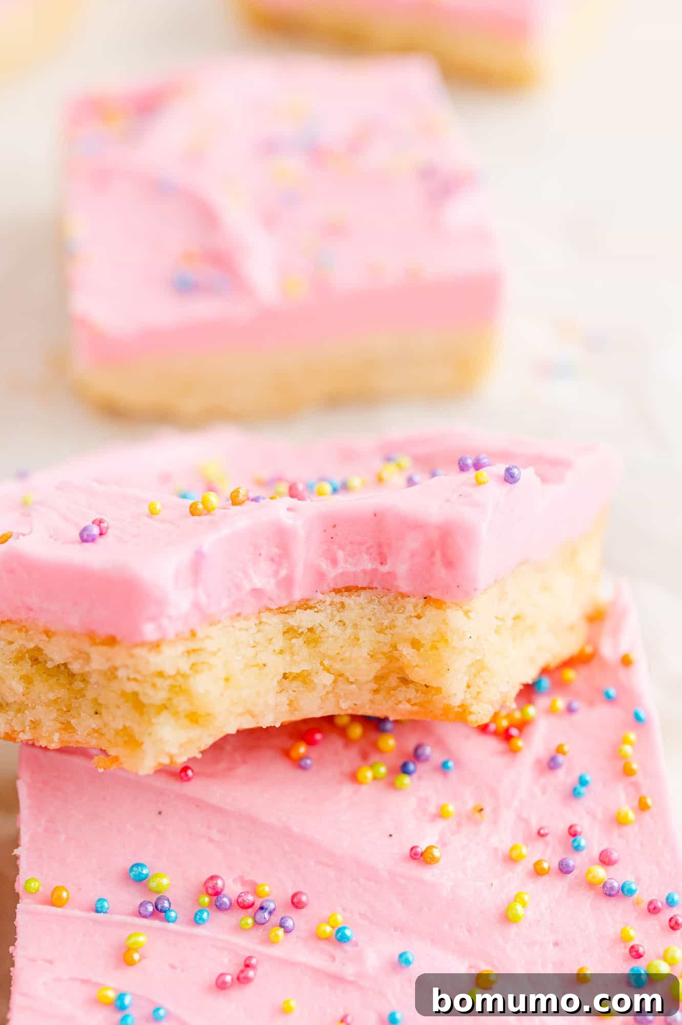 Cookie bar with pink frosting, showing a bite taken out to reveal its soft, chewy texture.