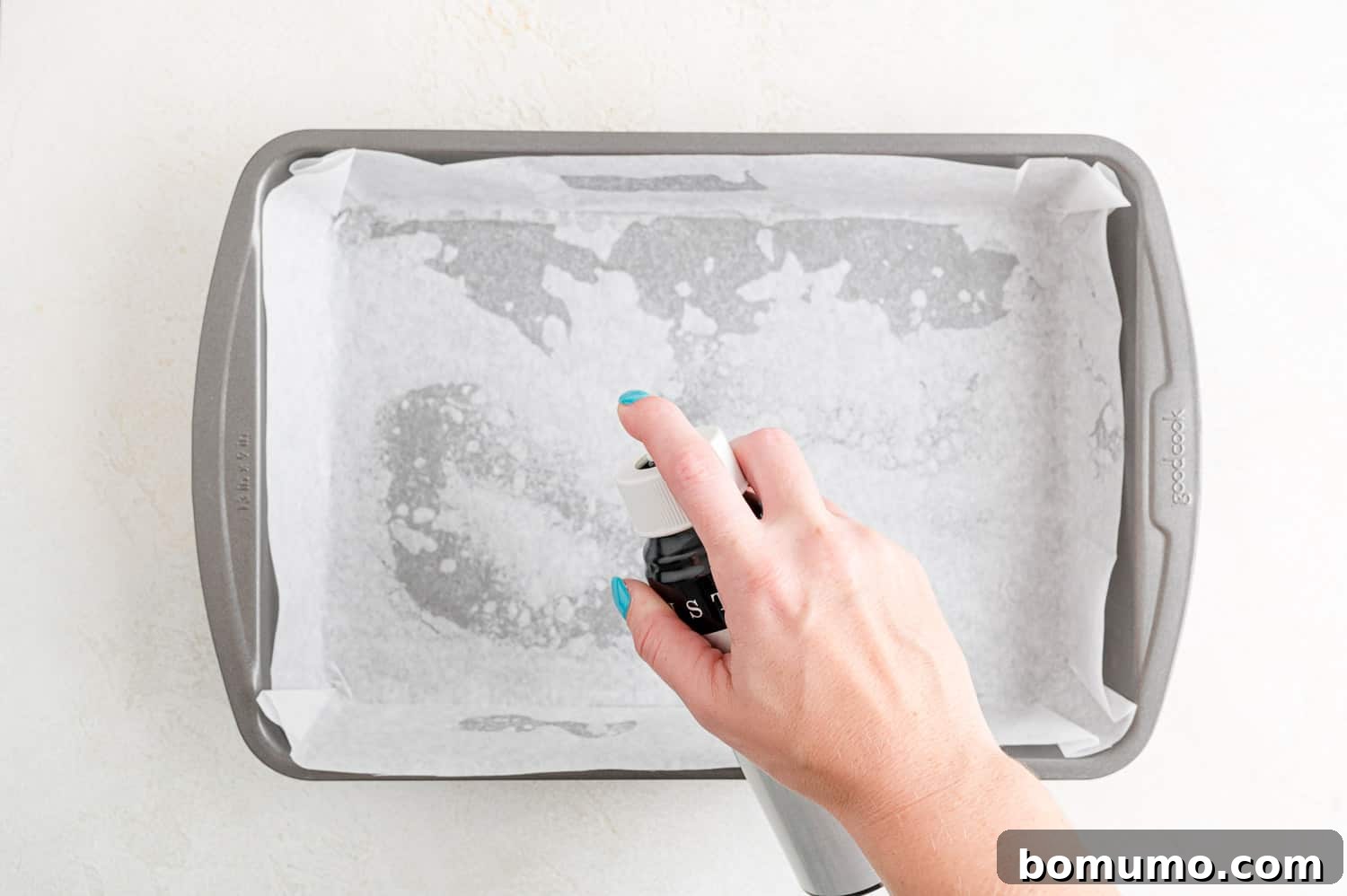 Parchment paper lined baking pan being sprayed with nonstick cooking spray, preparing for cookie dough.