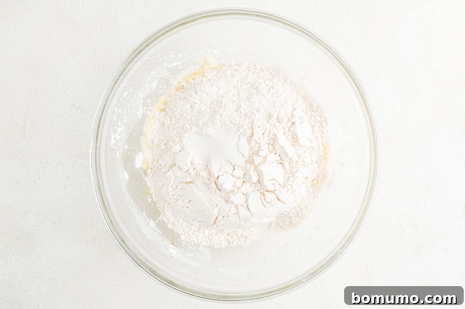 Flour mixture carefully added to the mixing bowl containing the wet ingredients for cookie dough.