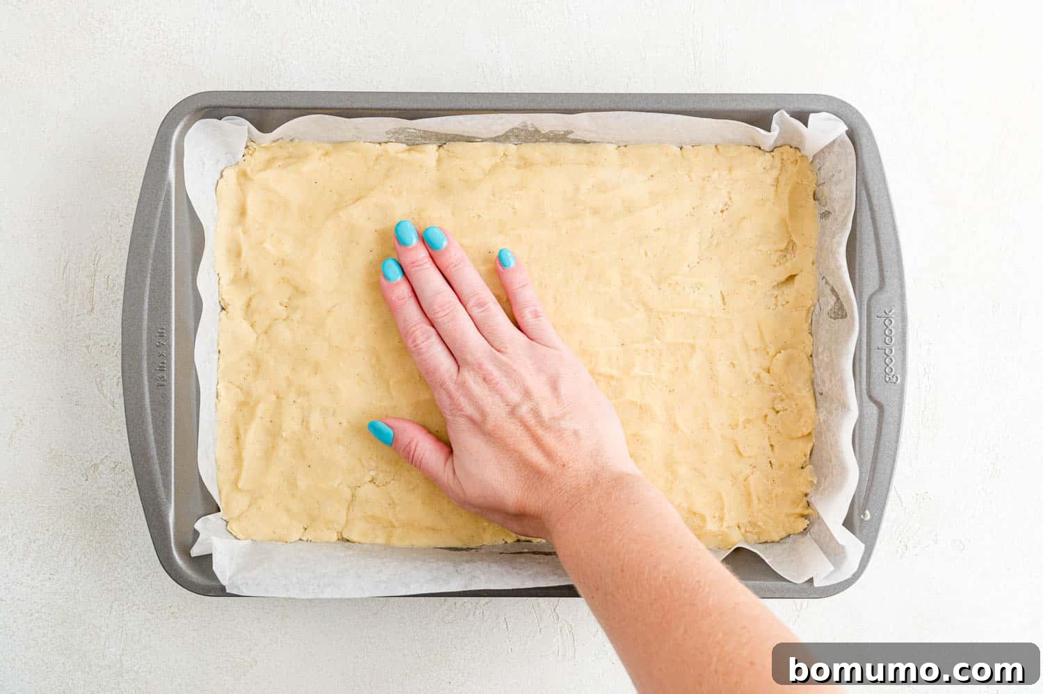 Cookie dough being pressed carefully and evenly into the prepared baking pan.