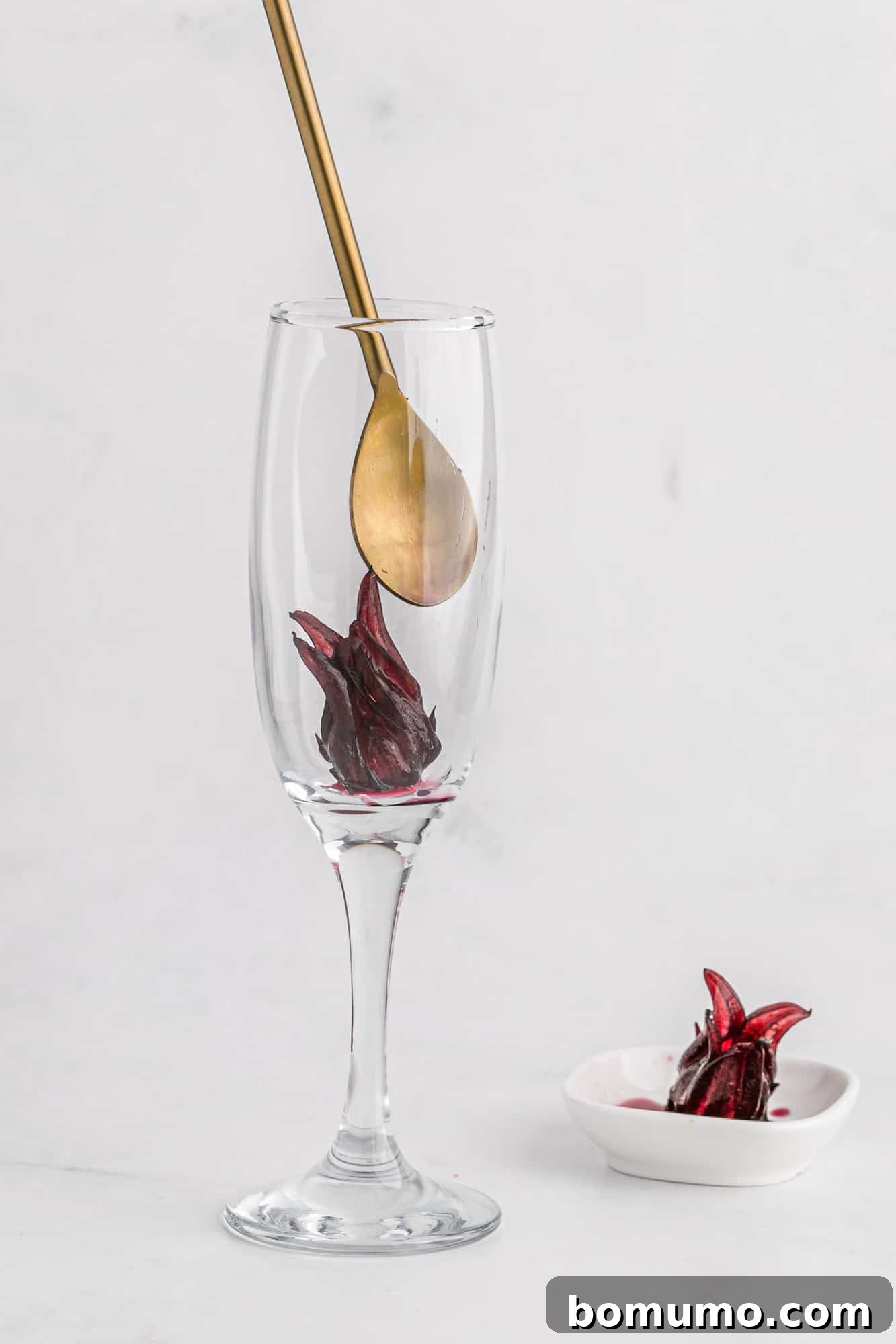A hibiscus flower being carefully placed into a champagne flute, ready for mixing.