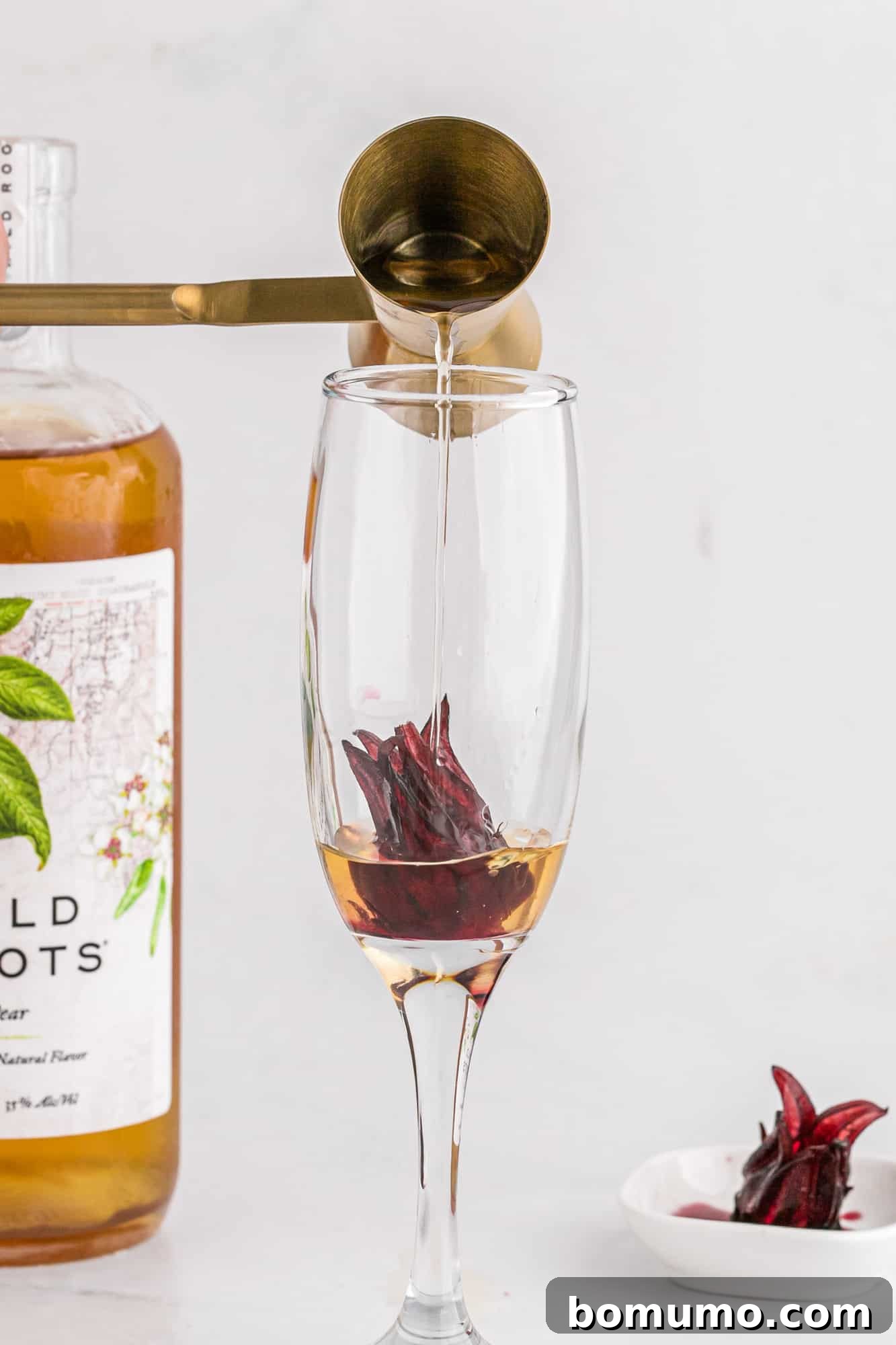 Pear vodka being poured into a champagne flute over a hibiscus flower.