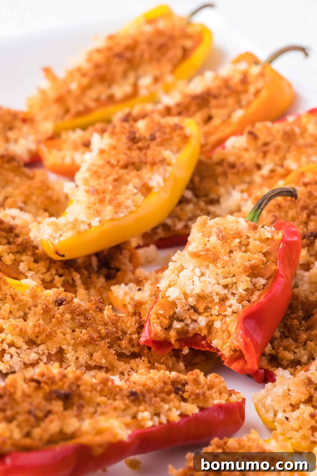 A single Southwestern stuffed mini sweet pepper, perfectly baked with a golden topping, showing a bite taken out to reveal the creamy filling.