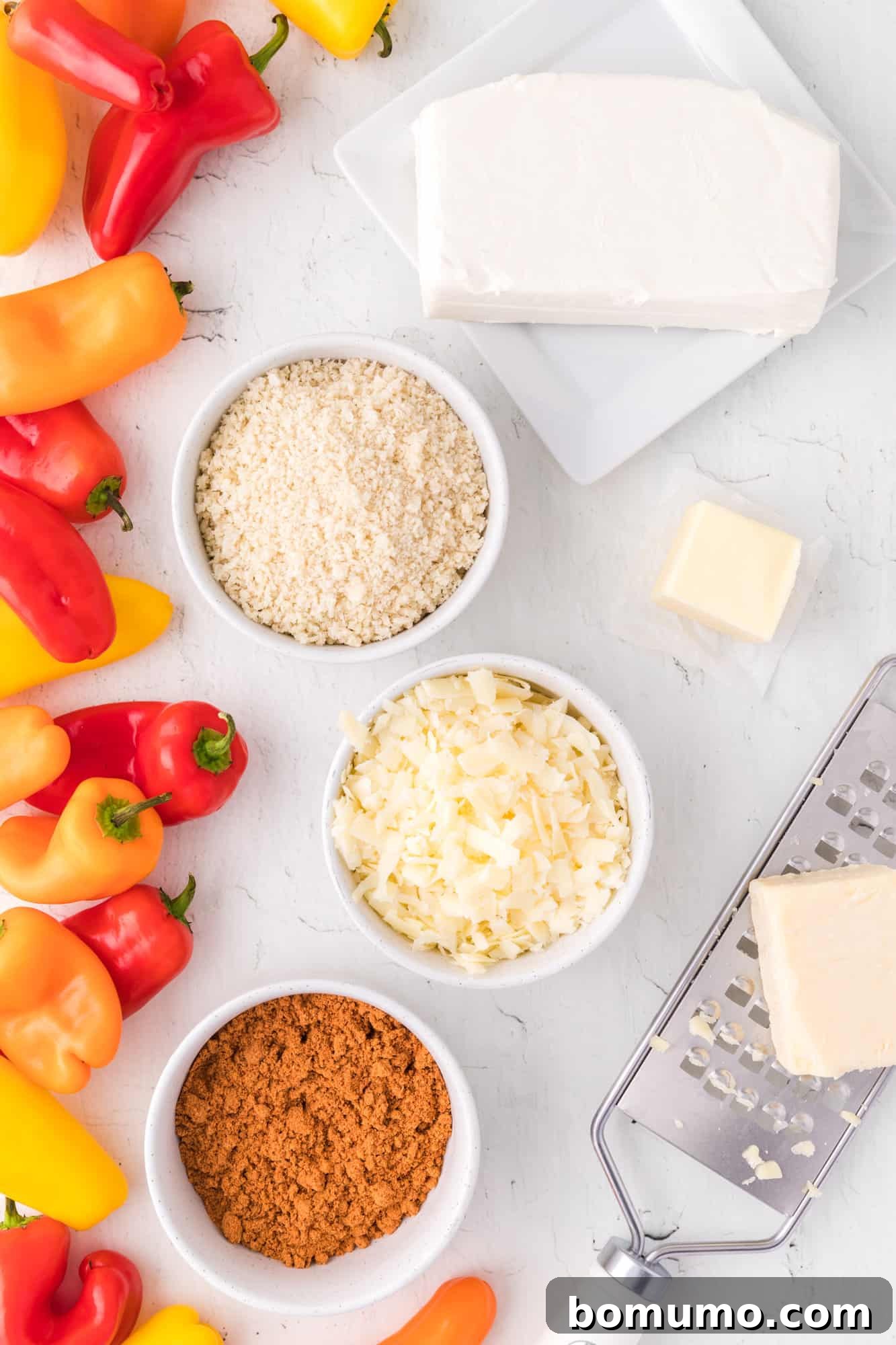 A colorful array of ingredients for mini stuffed peppers, including vibrant sweet mini peppers, cream cheese, shredded cheddar, taco seasoning, panko, and butter.