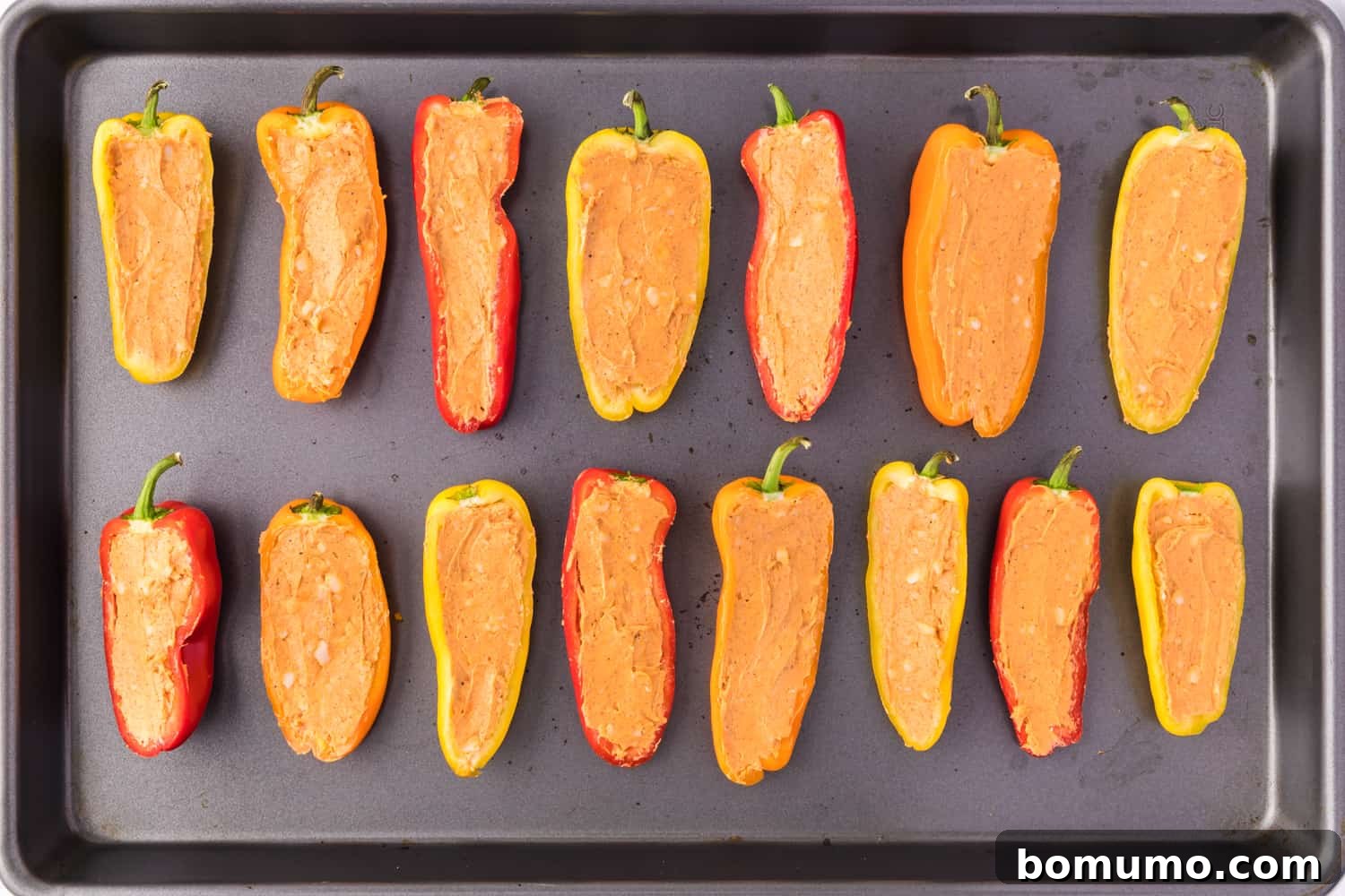 Rows of colorful mini peppers, expertly stuffed with the creamy cheese filling, laid out on a baking sheet.