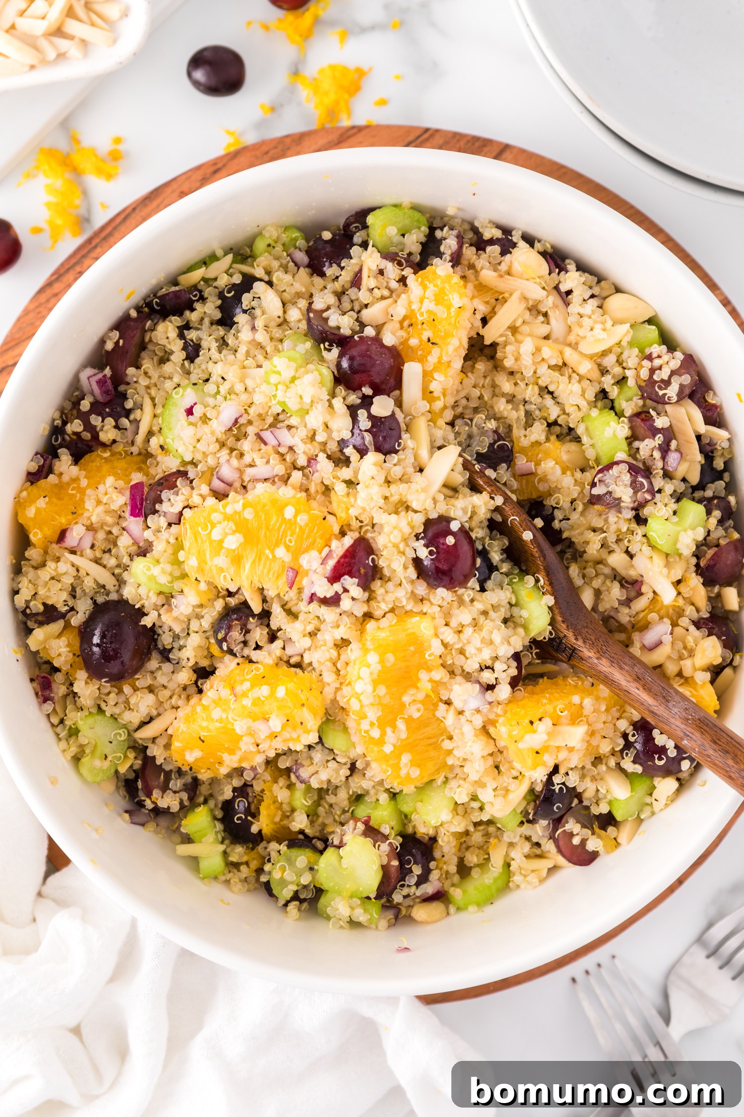 A large bowl brimming with a vibrant quinoa salad, artfully garnished with fresh oranges, juicy grapes, and crunchy almonds. This healthy and delicious salad is perfect for any season.