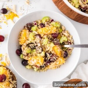 Quinoa salad with orange and grapes in a white bowl, a refreshing and healthy meal option.