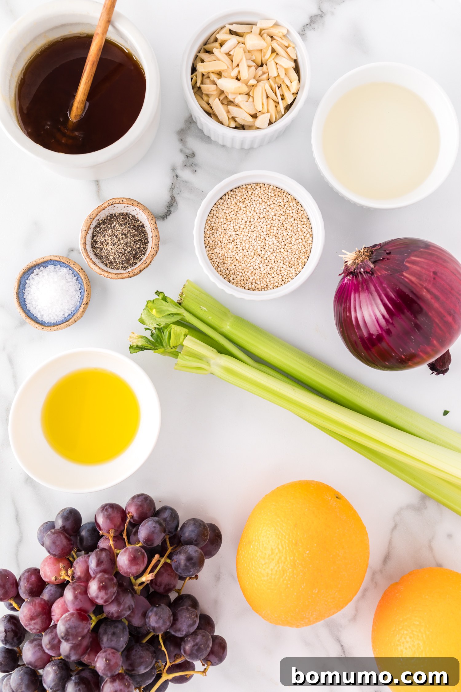 A collection of fresh ingredients laid out, including vibrant red grapes, crisp celery, a finely diced red onion, and unpeeled oranges, all ready for the quinoa salad preparation.