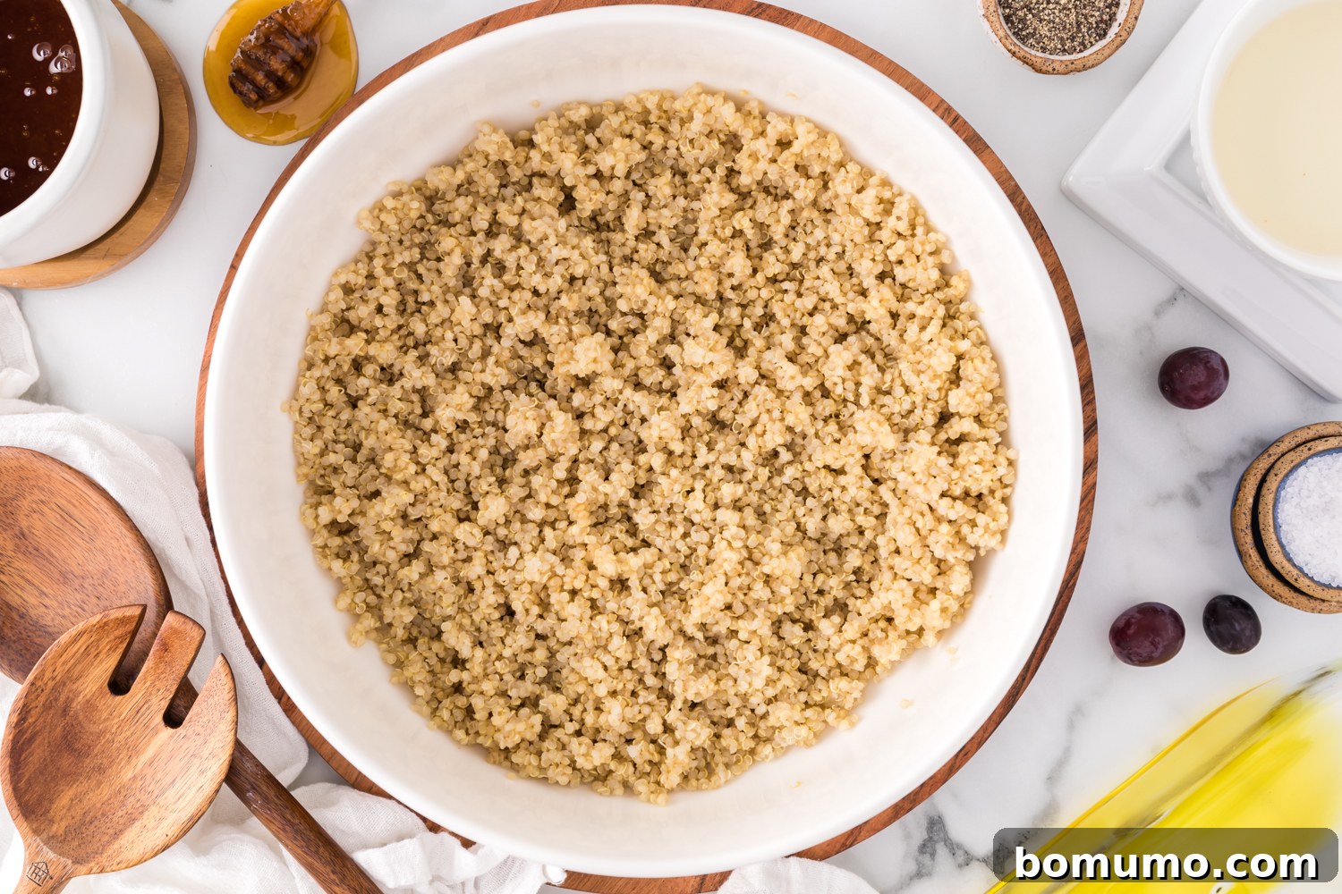 Cooked quinoa in a large bowl, surrounded by the fresh, colorful ingredients that will be added to the salad, awaiting assembly.