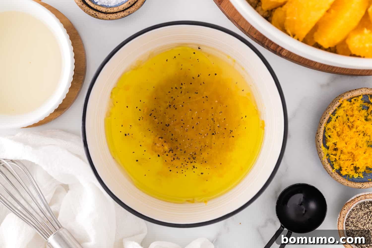 Individual ingredients for the orange vinaigrette, including olive oil, honey, and orange zest, placed around a small bowl of orange juice, awaiting mixing.