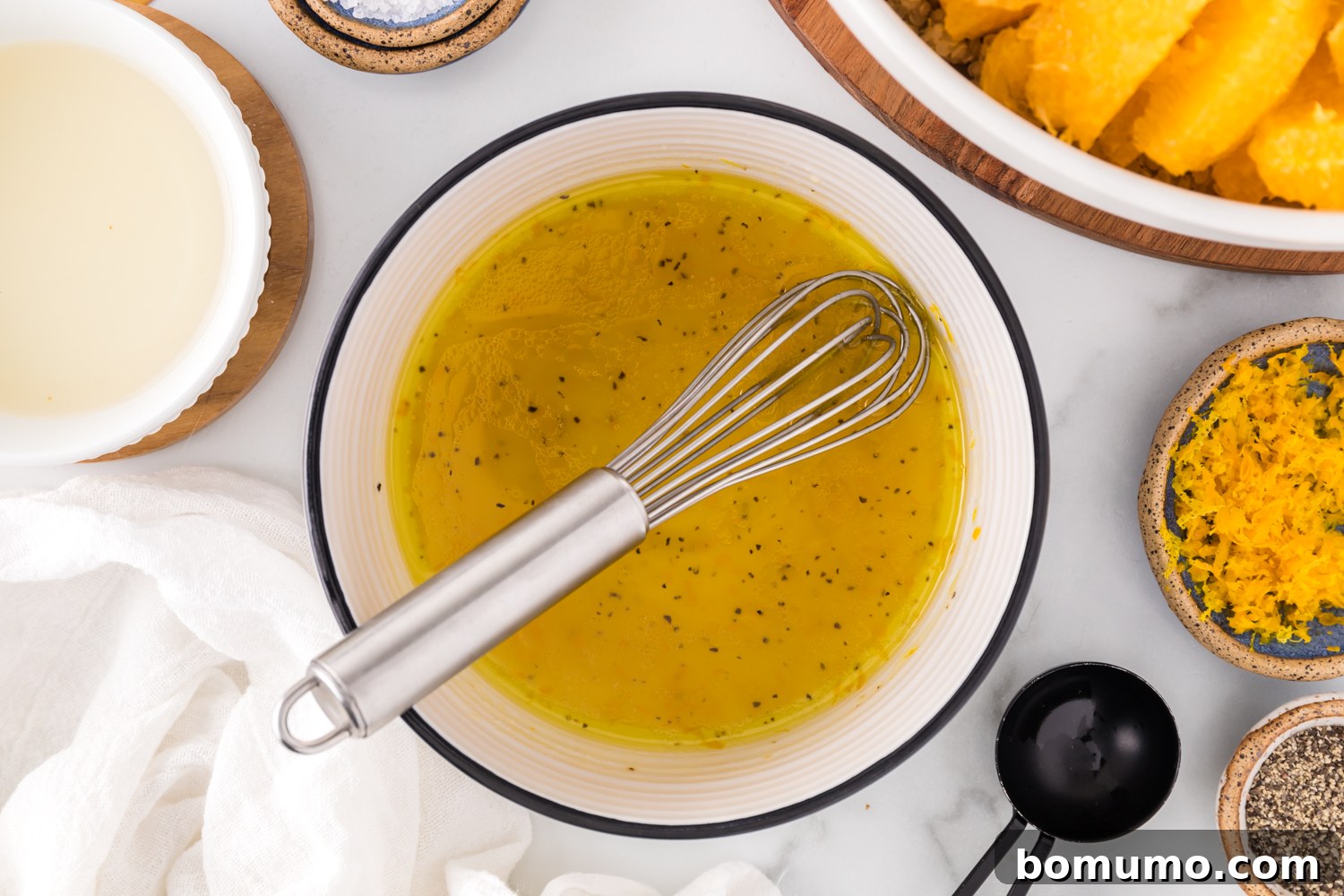 The freshly whisked orange vinaigrette in a small bowl, showcasing its smooth, emulsified texture, ready to dress the salad.