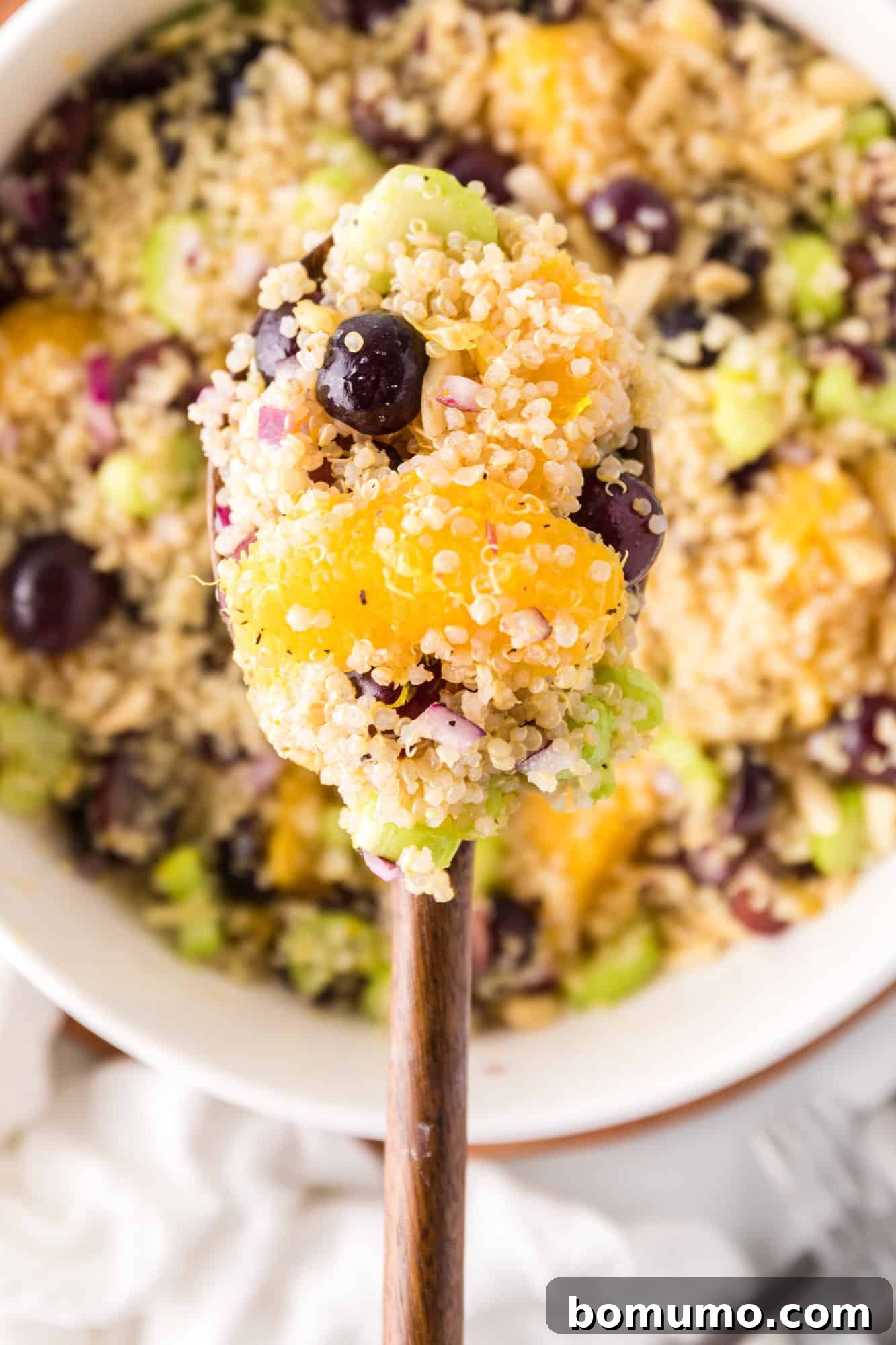 A serving spoon lifting a portion of the quinoa salad, highlighting its colorful ingredients and appealing texture, ready to be enjoyed.