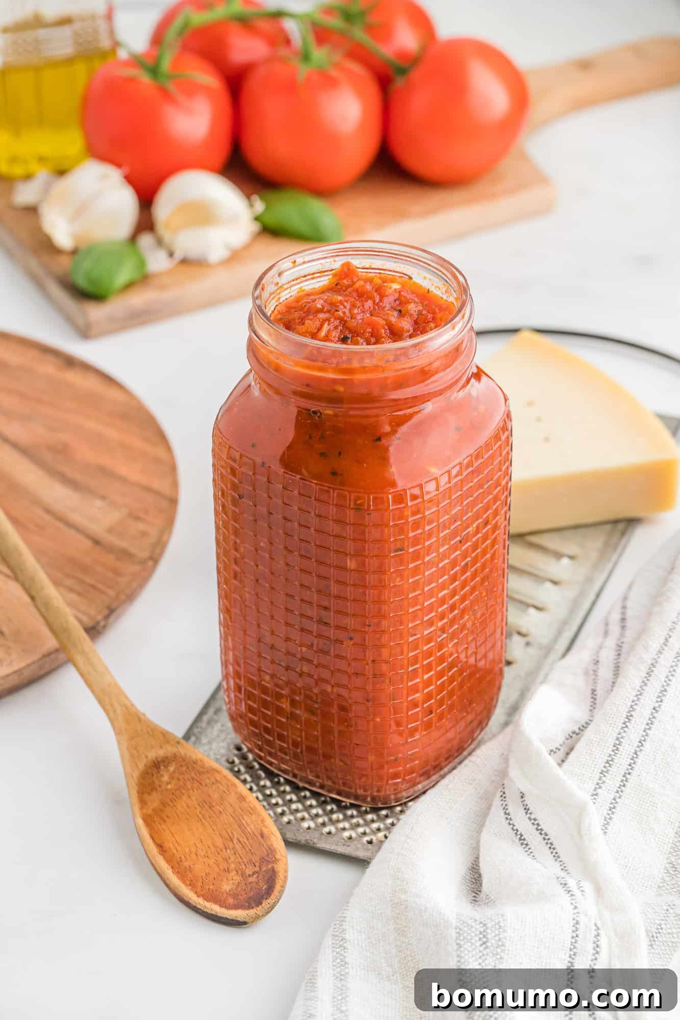 Homemade pizza sauce in a glass jar with fresh red tomatoes in the background, hinting at its natural ingredients.