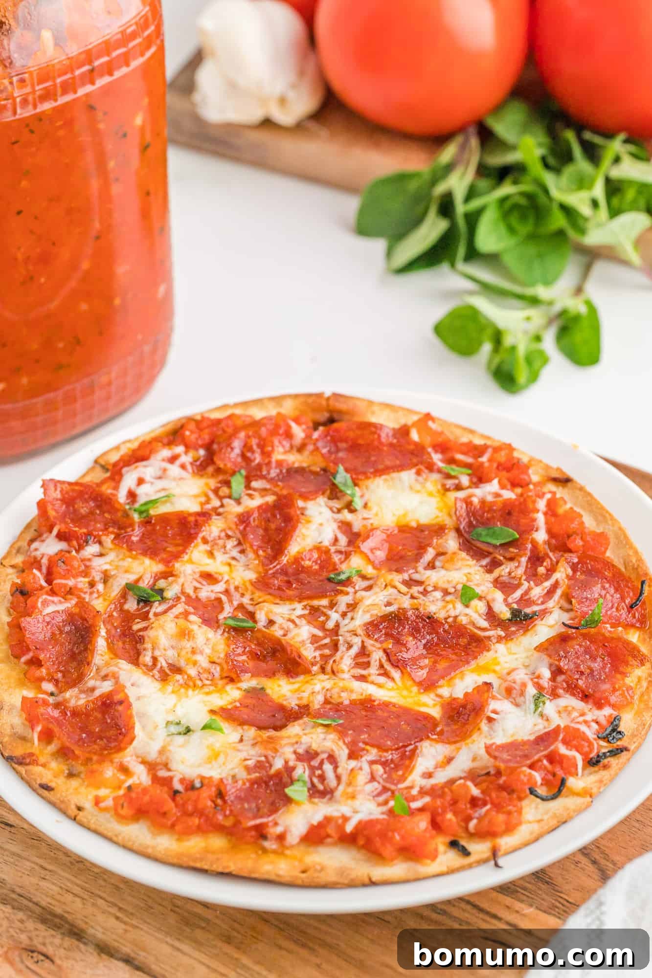 A delicious pepperoni pizza with rich, homemade sauce visible, sitting next to a jar of the same sauce.