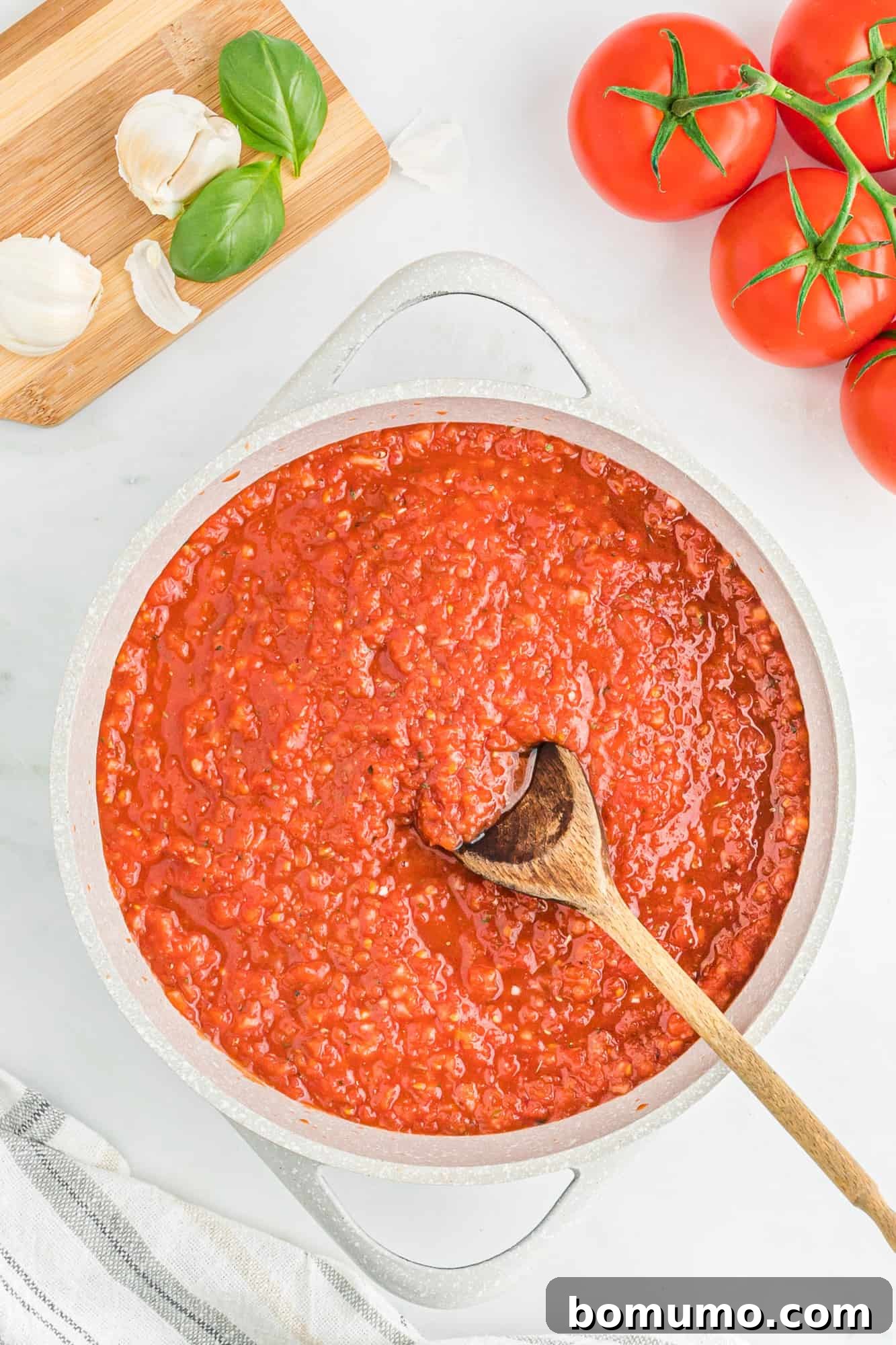 Smooth, rich pizza sauce simmering in a large white saucepan, stirred gently with a wooden spoon.