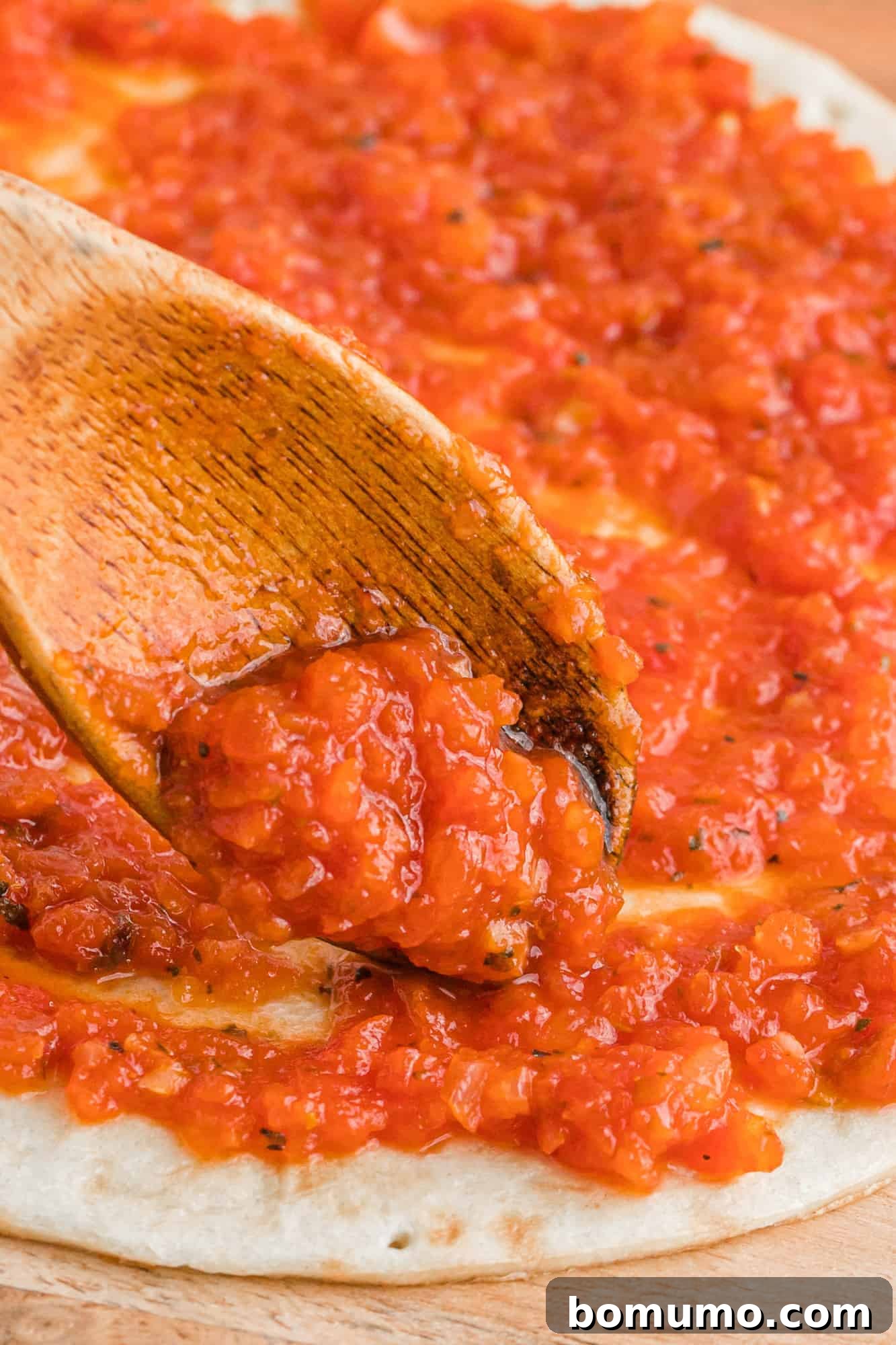 Delicious homemade pizza sauce being generously spooned onto a fresh pizza crust, ready for toppings.