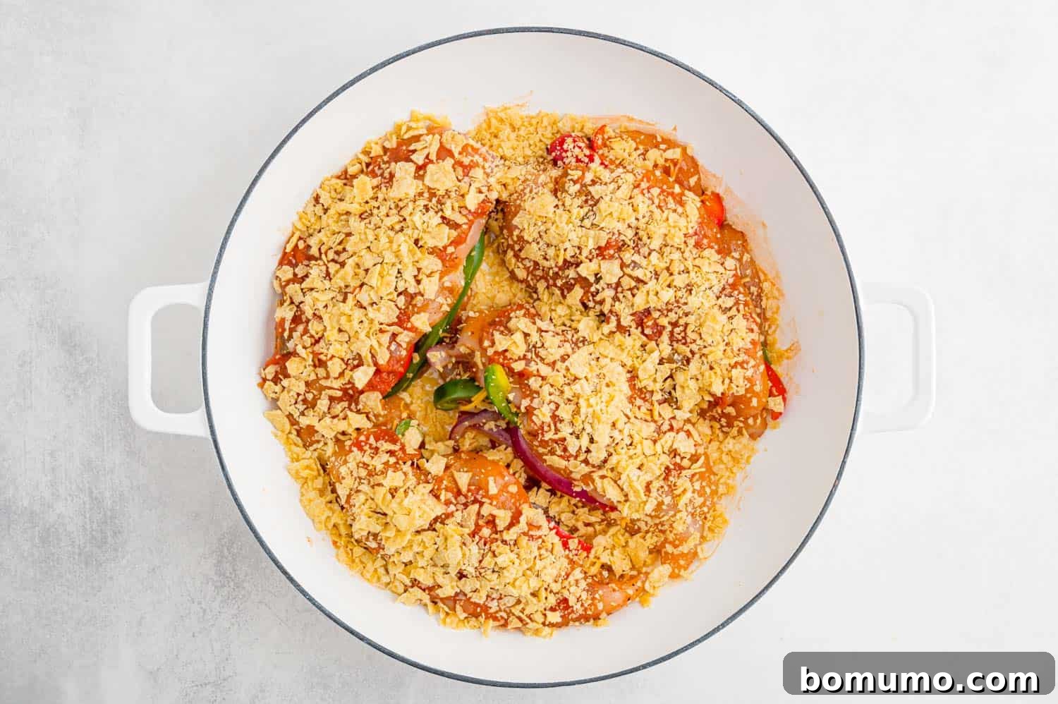 Unbaked fajita stuffed chicken breasts arranged in a baking dish, topped with salsa and crushed tortilla chips.