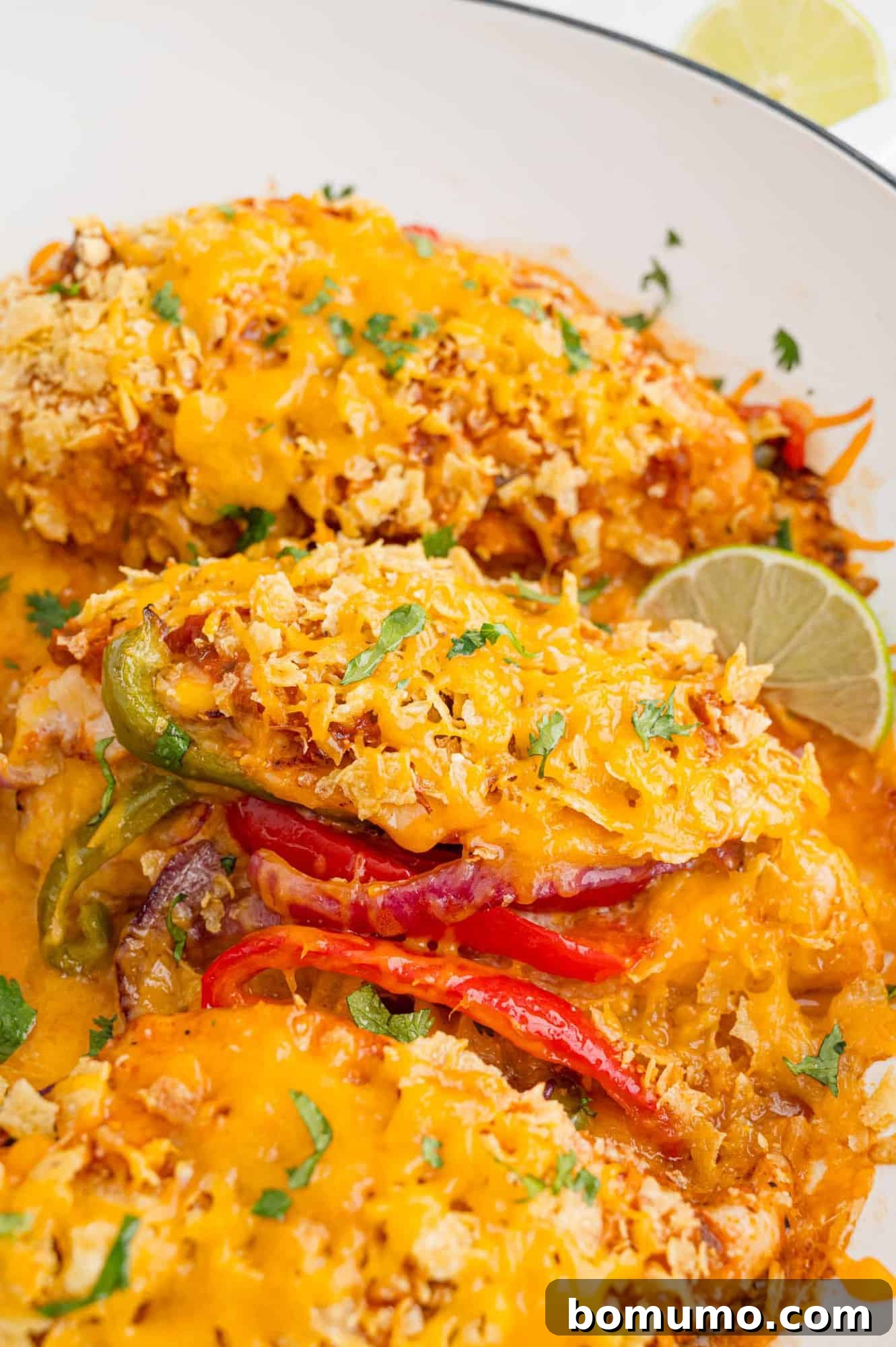 Close-up of a chicken breast generously stuffed with peppers and onions, topped with crushed chips and melted cheese.