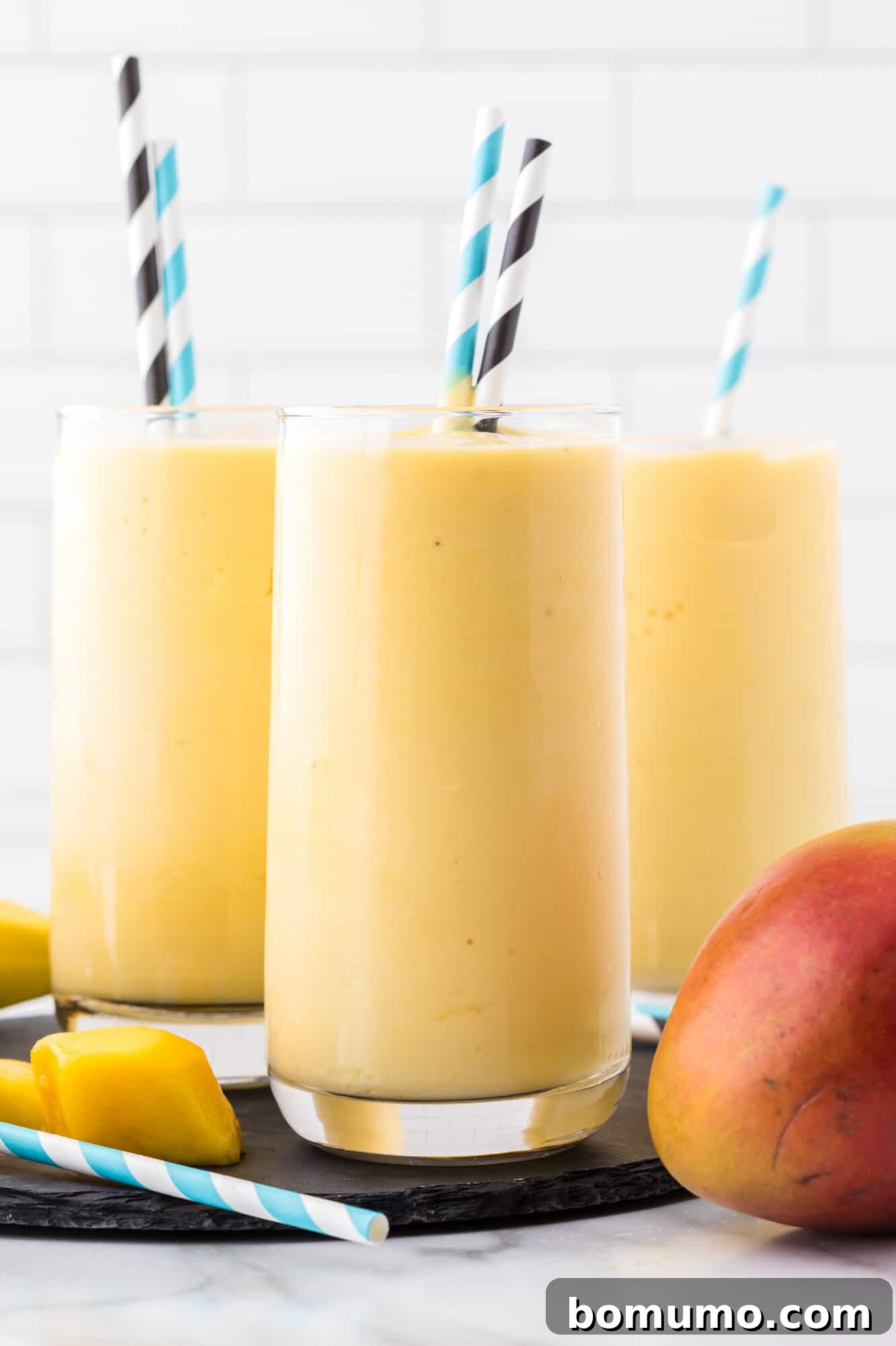 Three mango smoothies with paper straws.