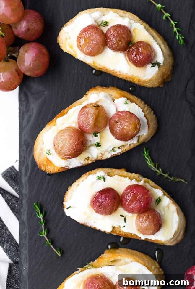 Image of roasted grape crostini on a black slate background. Fresh thyme is sprinkled around them.
