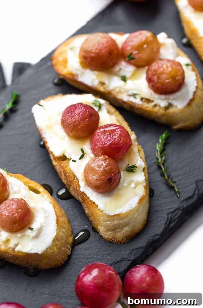 Image of crostini on a black slate board. It is stopped with ricotta cheese, roasted grapes, honey, and thyme.